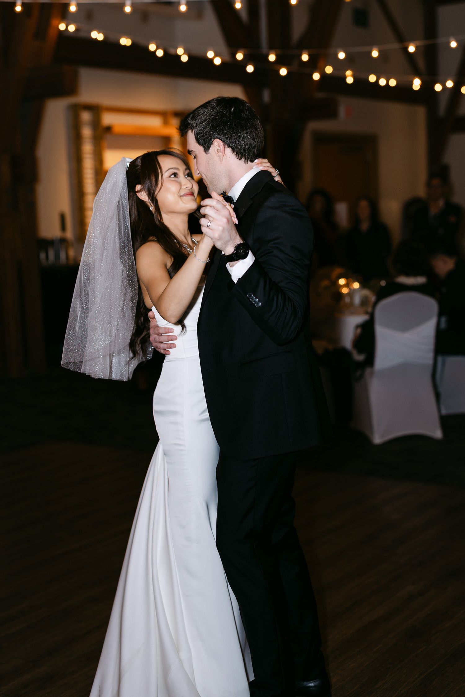 Bride and groom share their first dance under string lights at elegant wedding reception venue.
