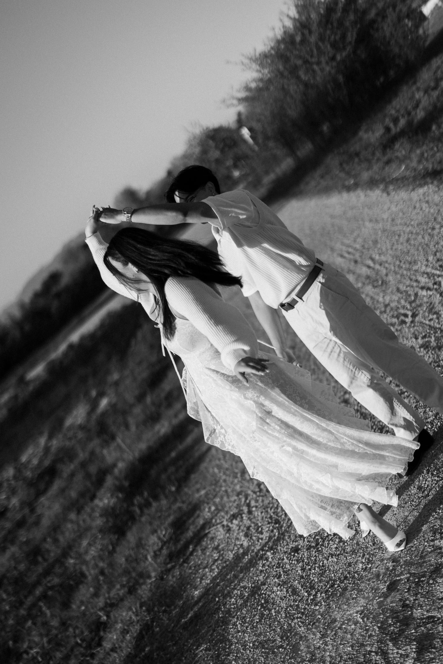 Black and white photo of a couple dancing in a grassy field, the woman in a flowing lace dress leaning back in a dip.
