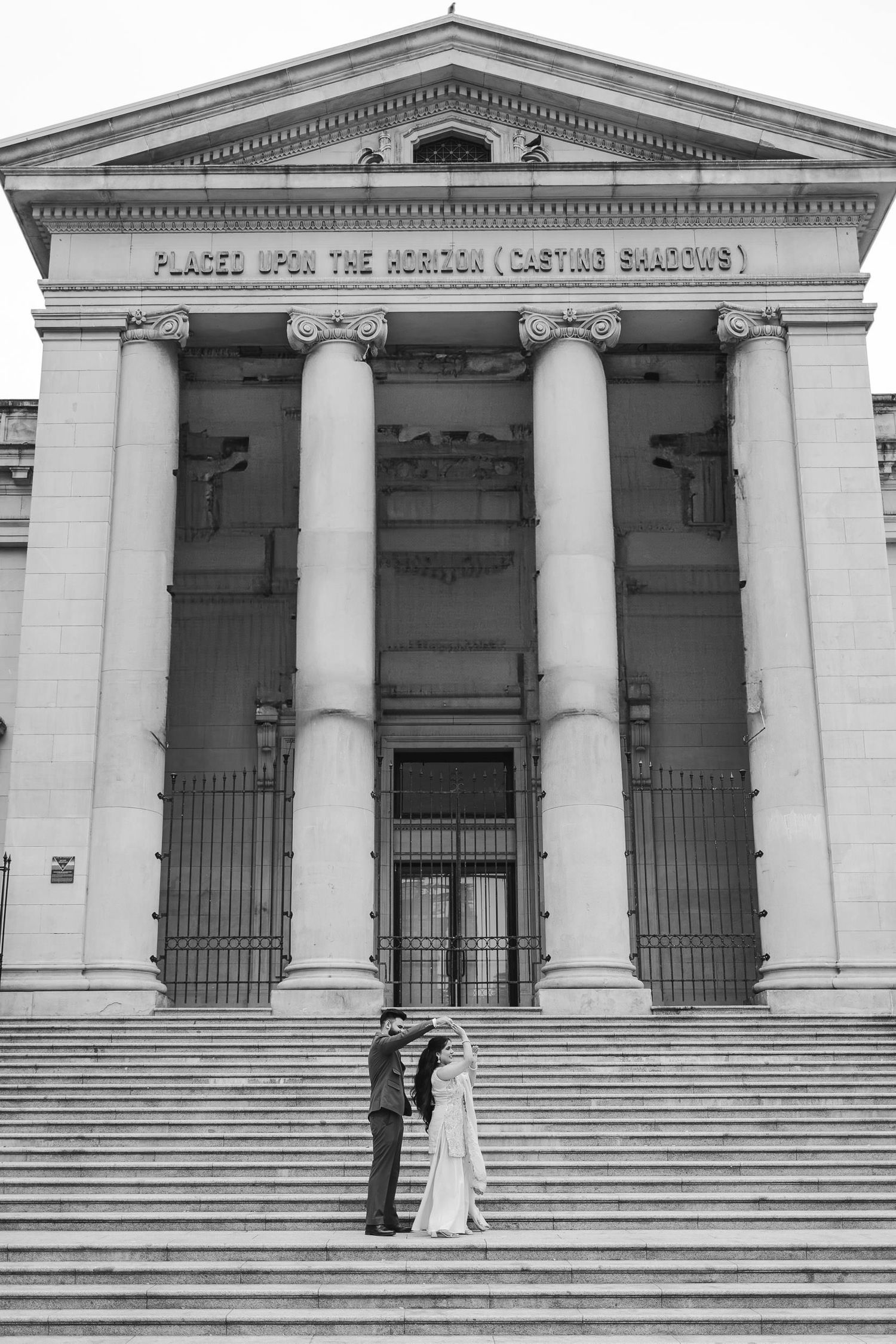 A wedding couple standing on grand stone steps of a neoclassical building with columns.