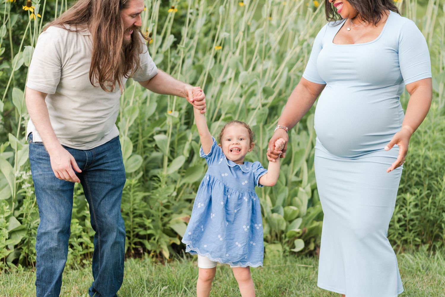 A family walks together through tall green corn stalks on a summer day at a farm.
