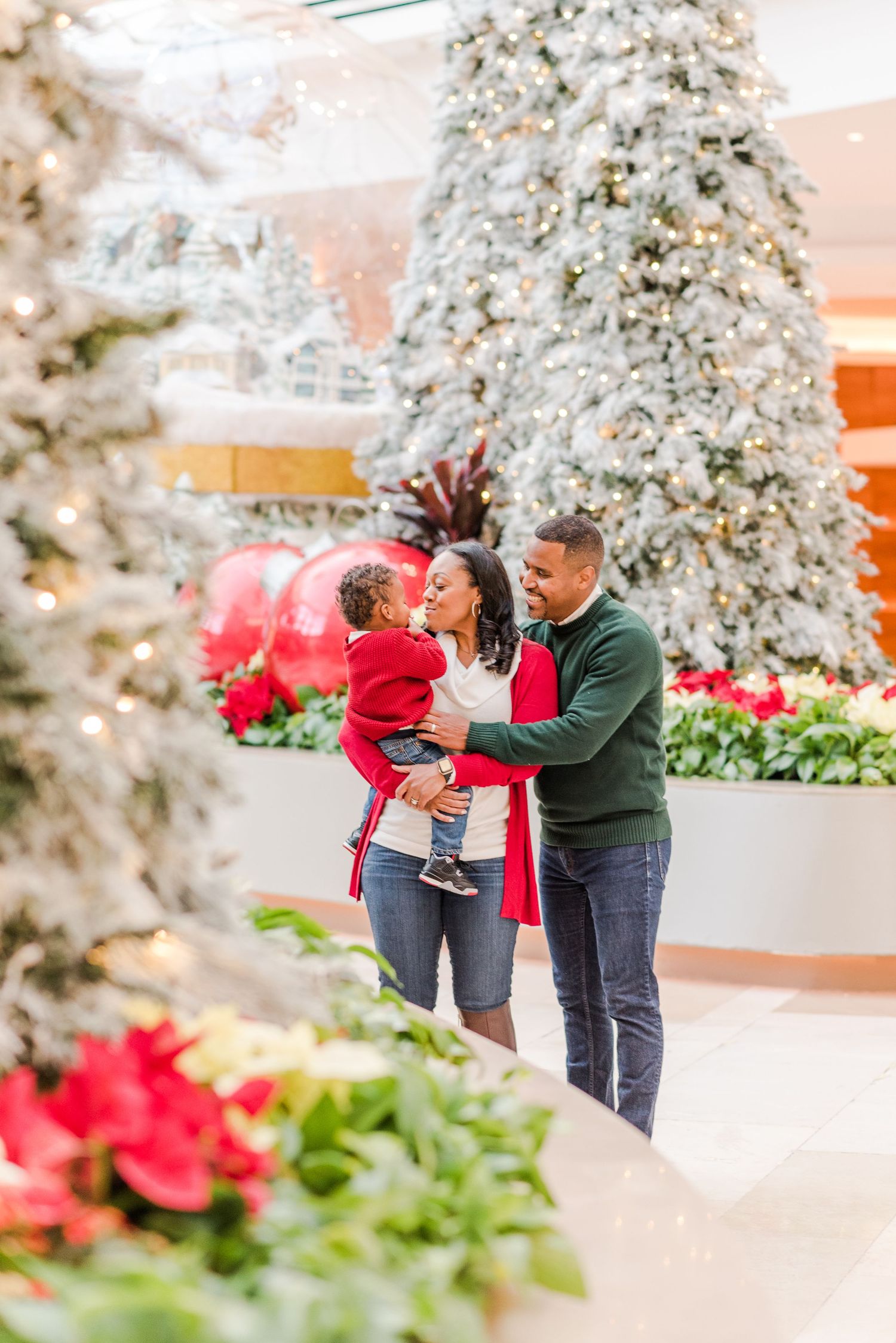 A couple embraces among holiday decorations with snow-covered trees and red poinsettias.