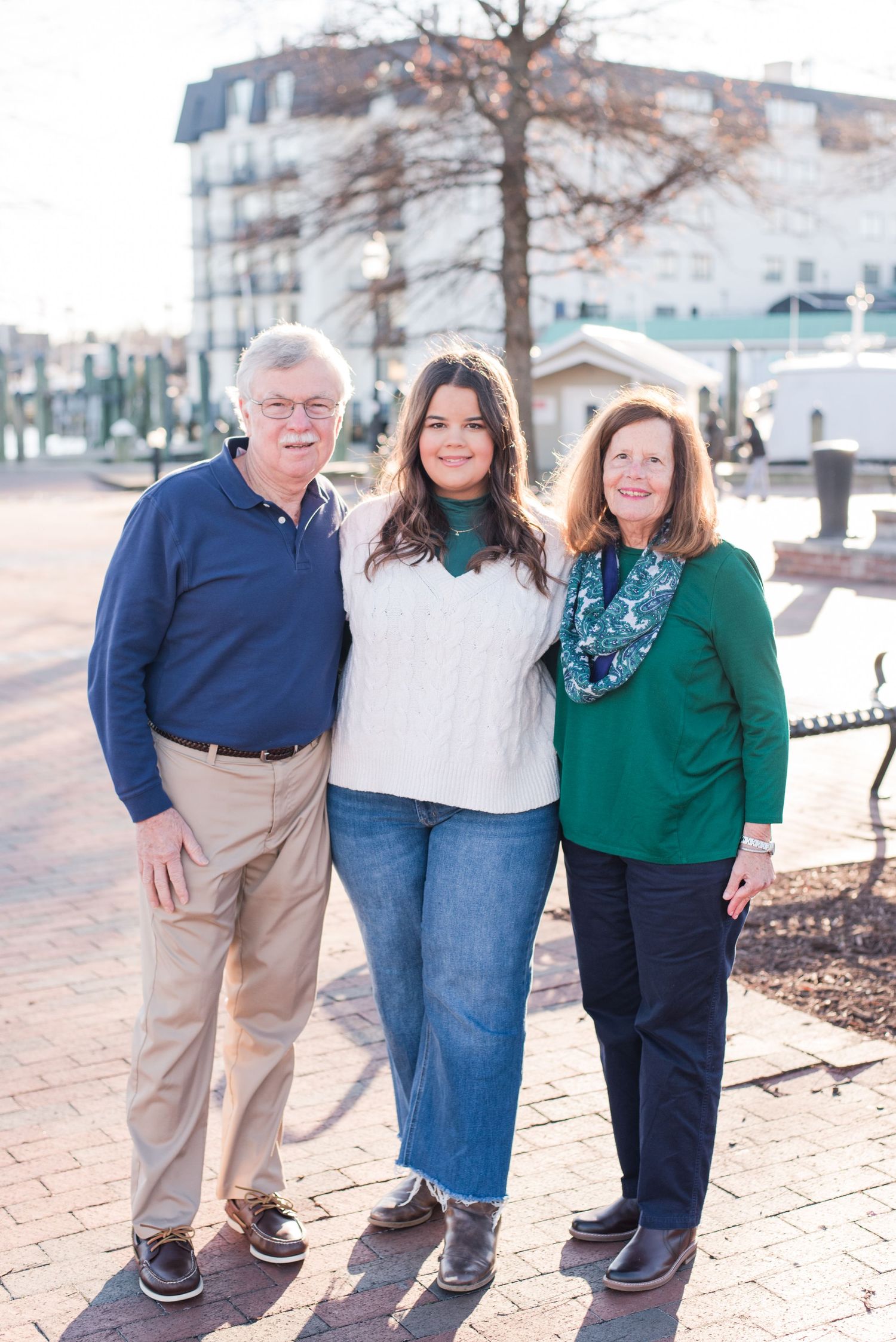 Three people stand together on a brick walkway on a sunny day wearing casual clothing.