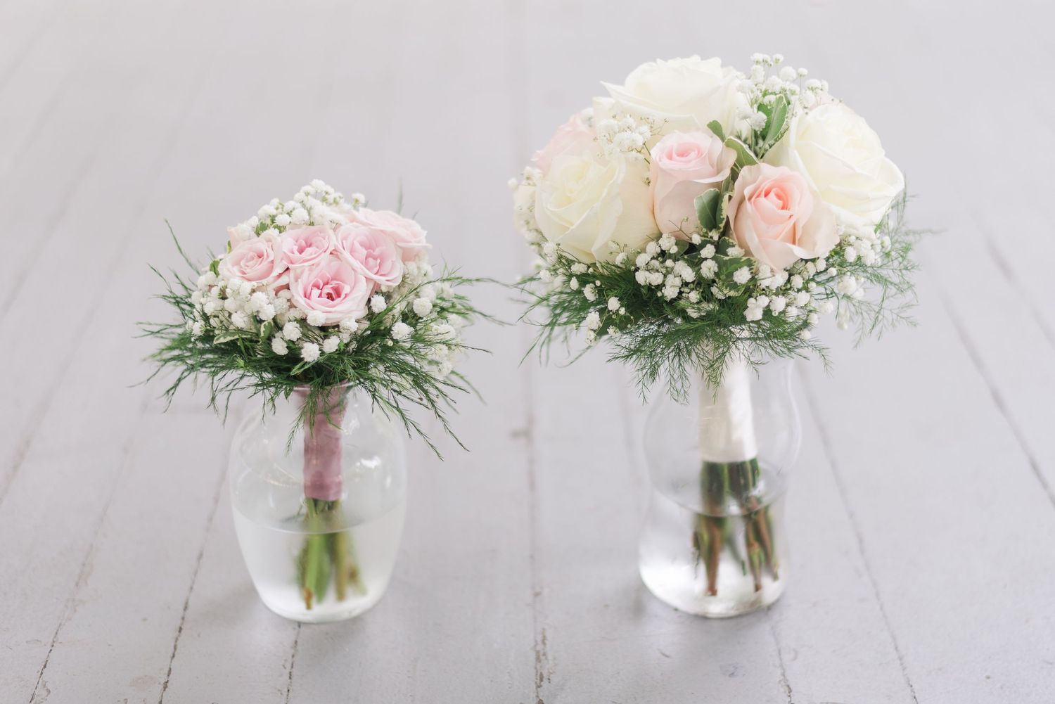 Two delicate flower arrangements with pink and white roses in glass vases on a gray surface.