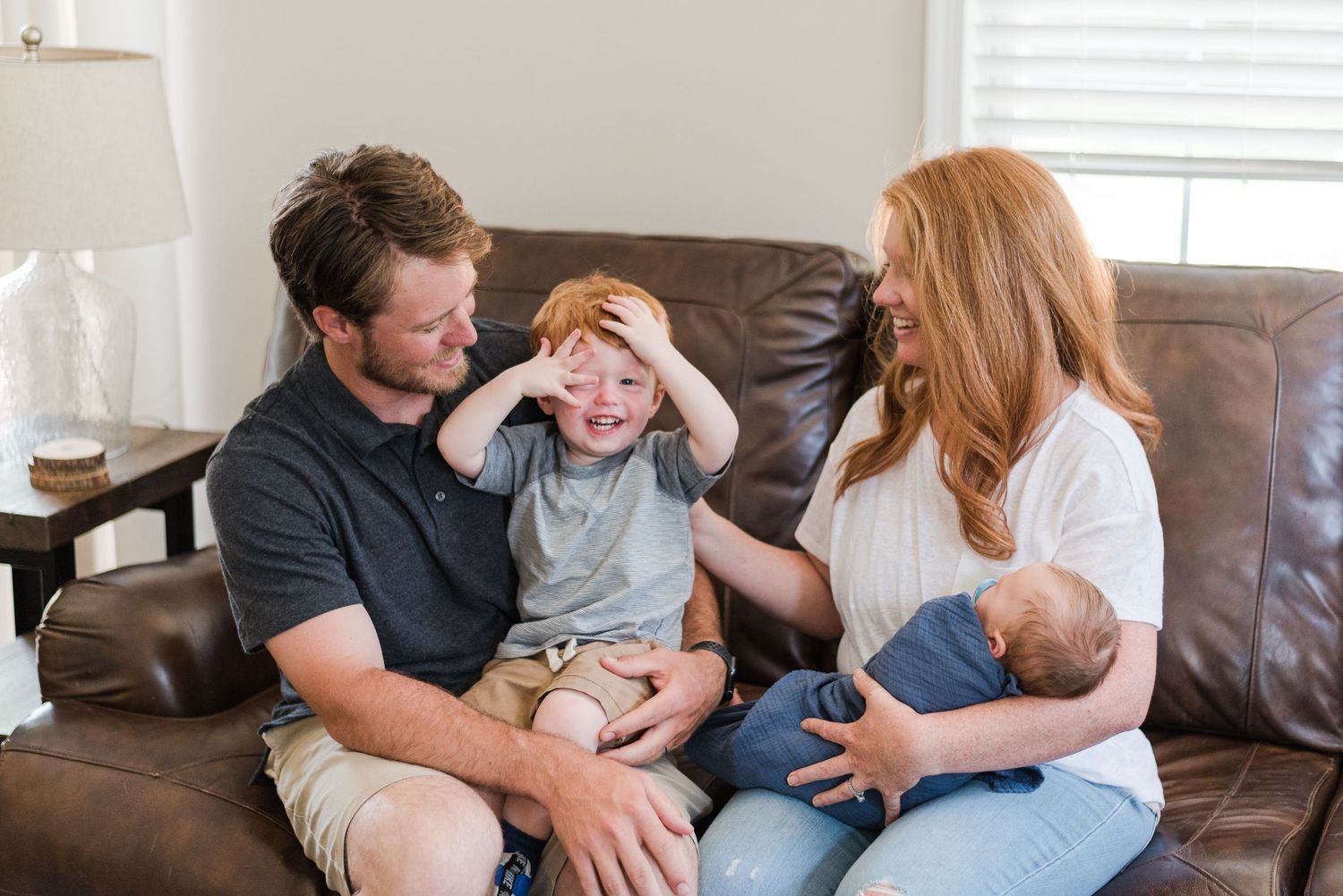Family enjoys a playful moment together while sitting on brown leather couch in living room.
