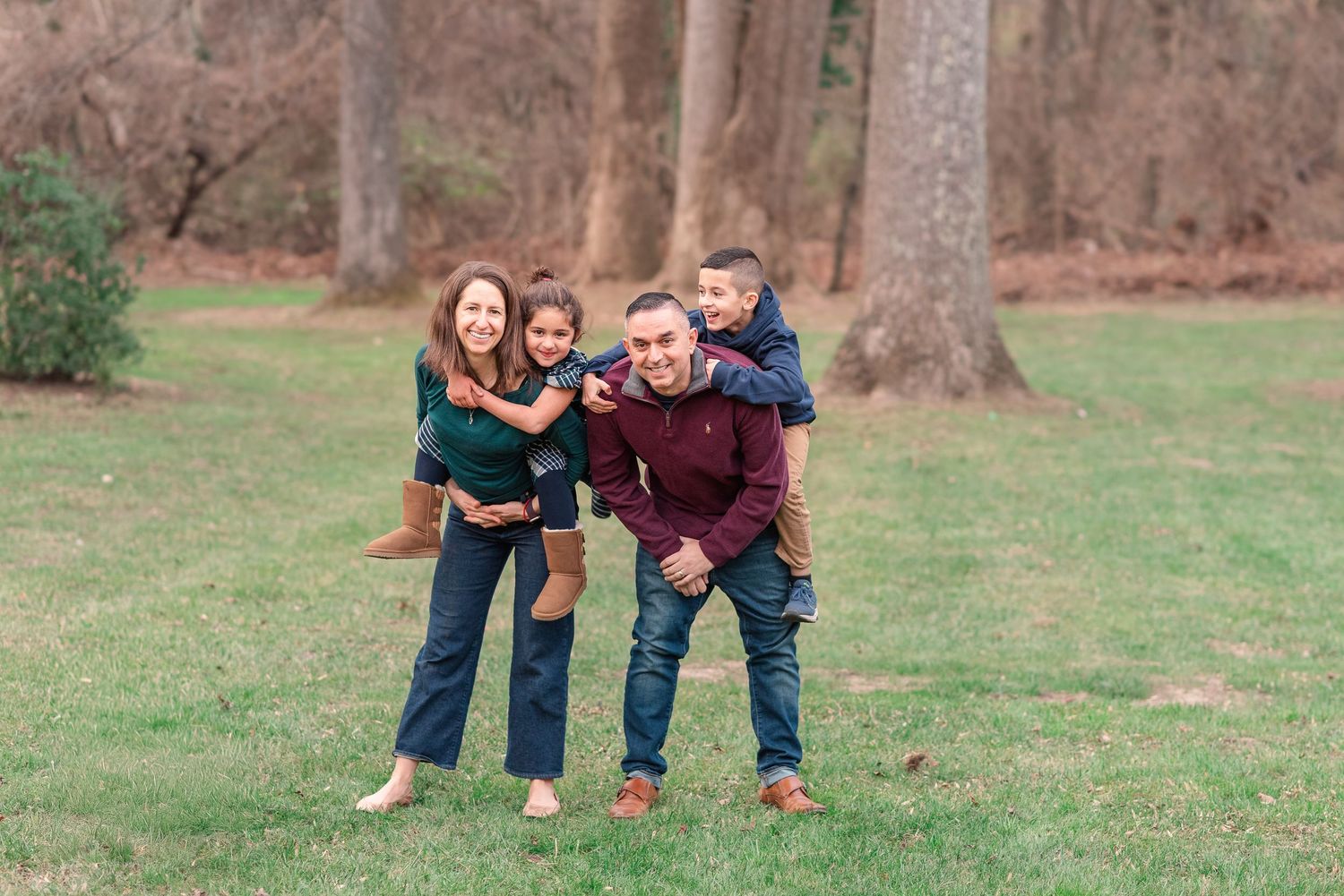 Family members in matching burgundy and navy outfits pose playfully together in an outdoor autumn setting.