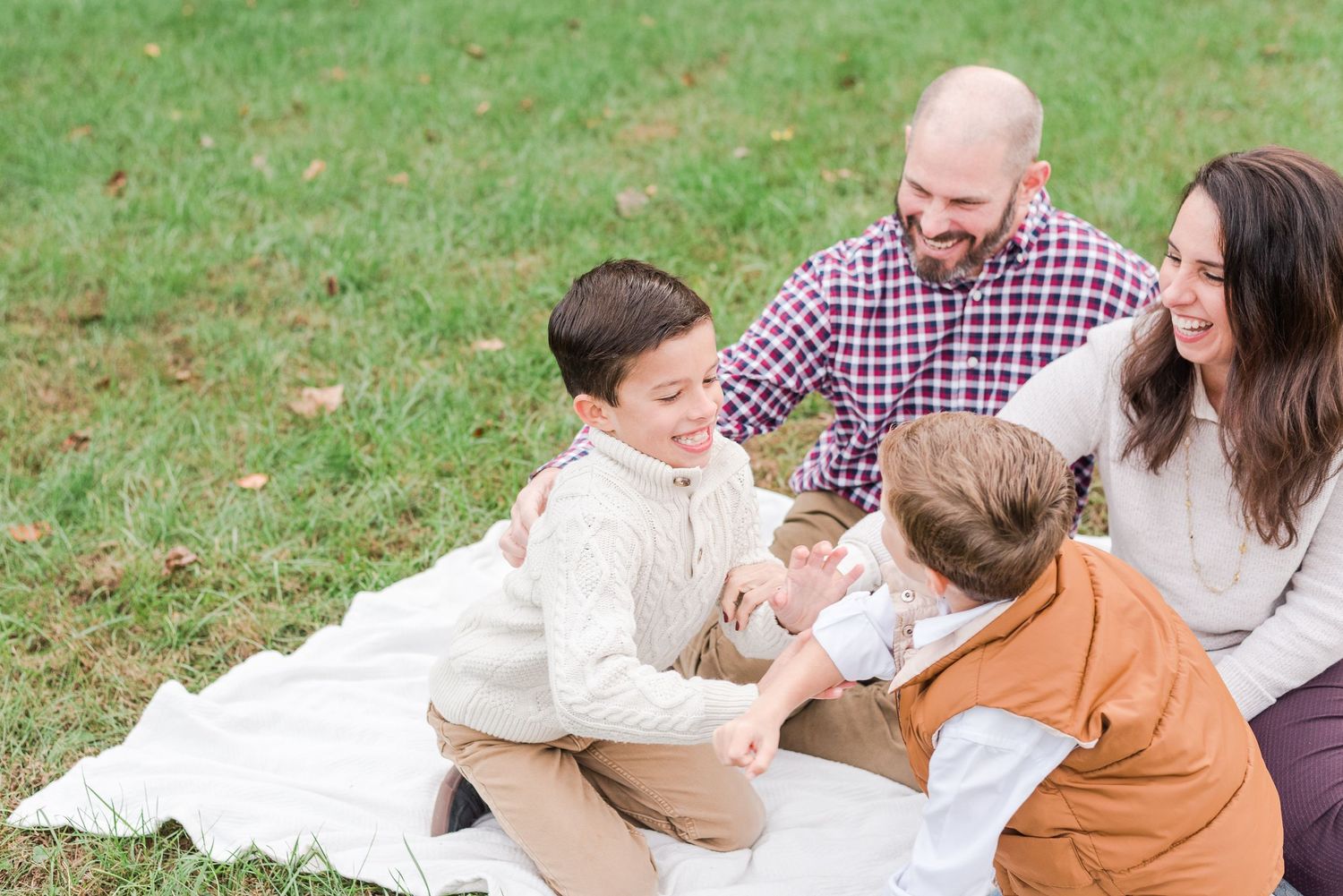 Family enjoying quality time together while sitting on a white blanket in grass during an outdoor photoshoot.