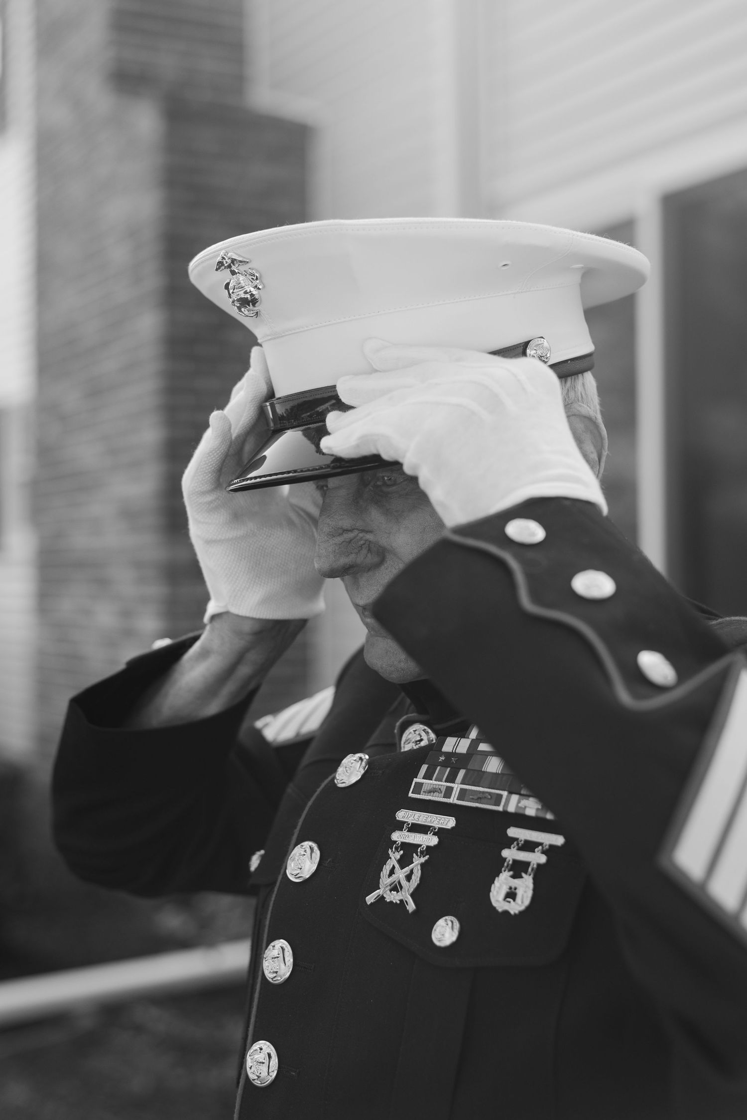 Black and white photo of a U.S. Marine adjusting his dress uniform cap displaying medals on his jacket.