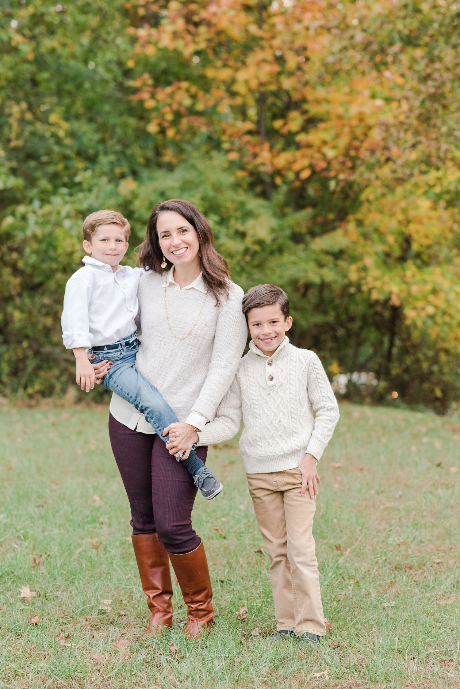 Family outdoor portrait with autumn foliage backdrop and coordinated casual outfits.