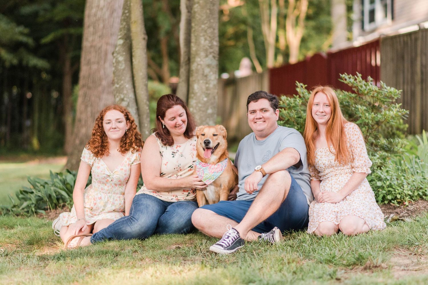 A happy group relaxes outdoors on the grass with their smiling golden mixed breed dog wearing a colorful bandana.