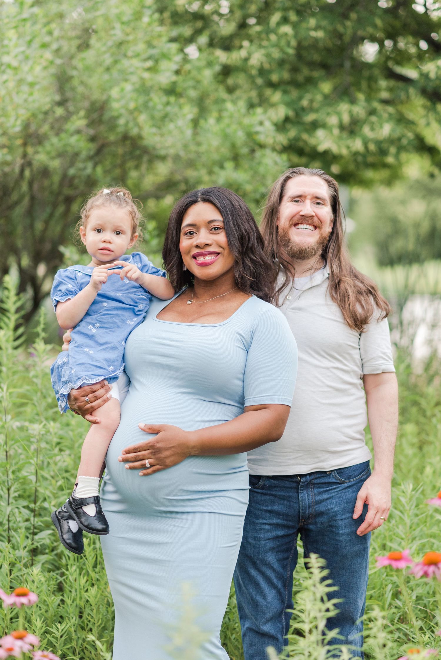 A family shares joyful moments together in a lush garden setting with blooming wildflowers on a sunny day.