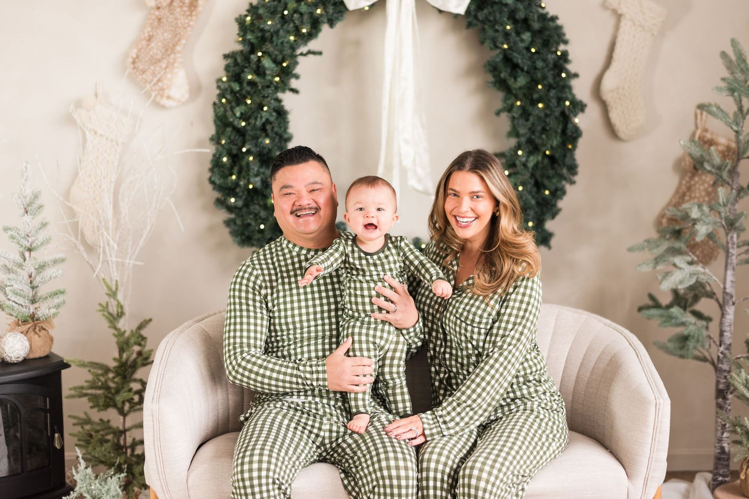 A family wearing matching green and white gingham outfits poses together in a holiday setting with garland decorations.