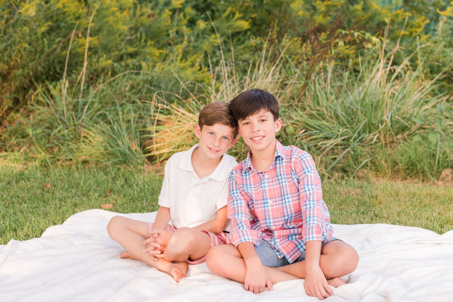 Two people sitting together on a white blanket outdoors with natural foliage in the background.