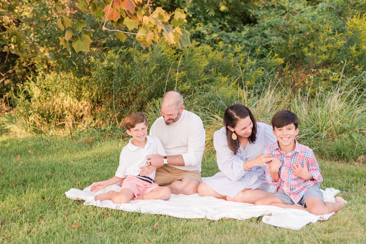 People lounging on a white blanket in a grassy field during golden hour.