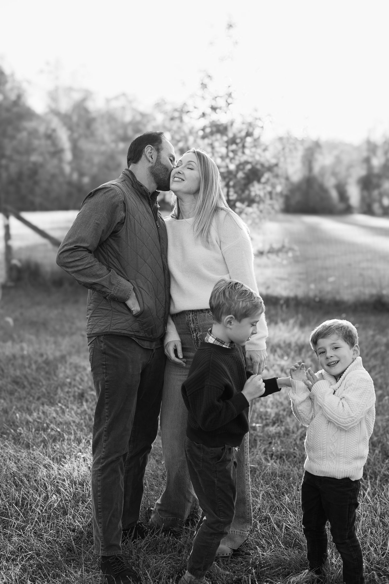 Black and white photo series of a young child covering eyes while couple shares intimate moment in outdoor setting.
