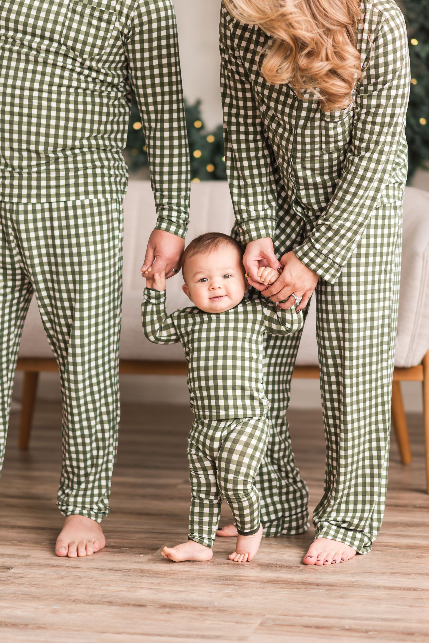 Family wearing matching green and white gingham pajamas standing together on hardwood floor.