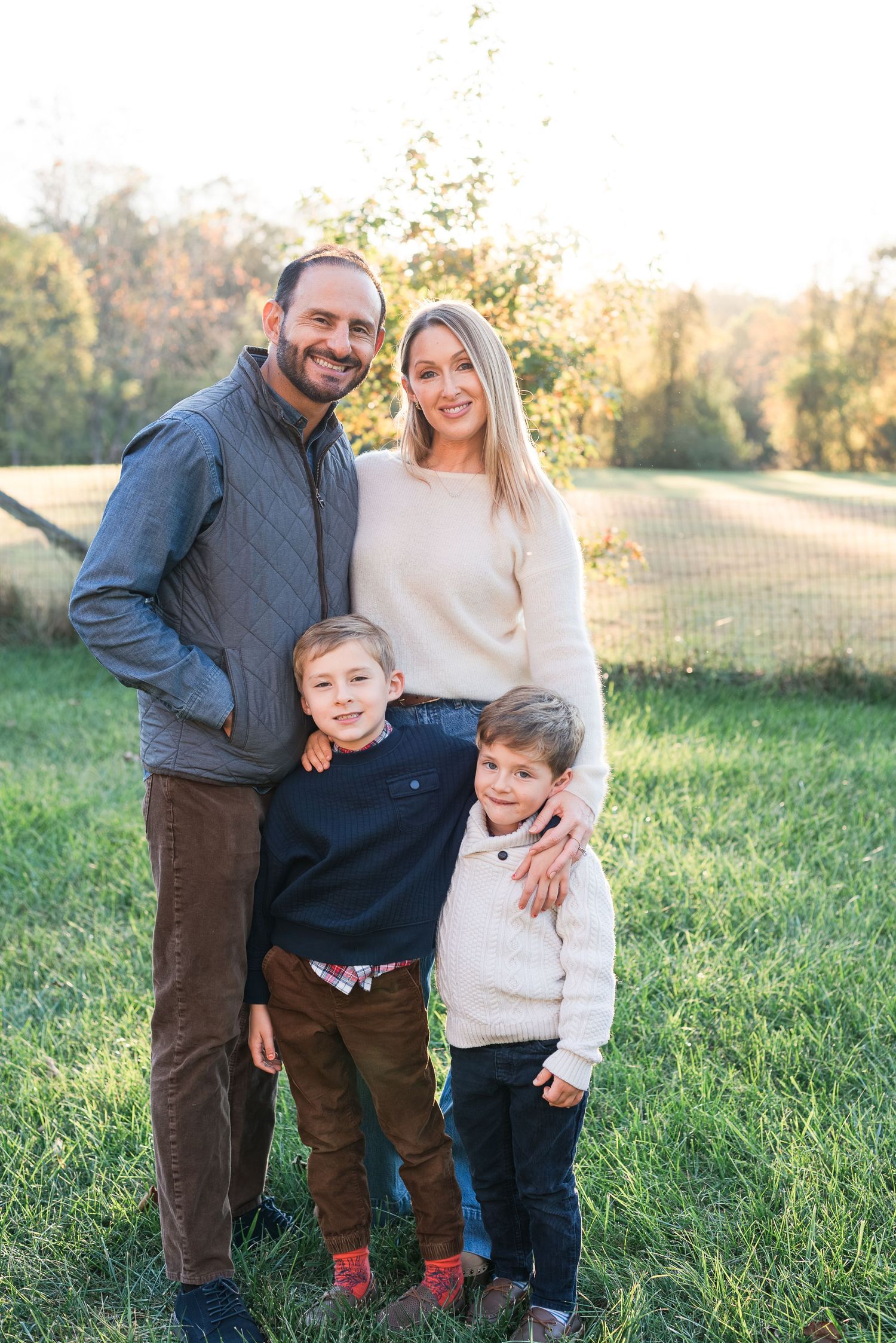 A family of four poses together outdoors in a grassy field during golden hour on an autumn day.