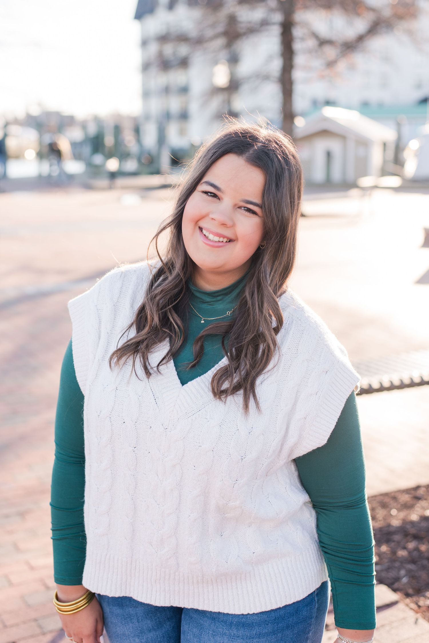 Outdoor fashion portrait featuring a cozy white knit sweater vest layered over a green turtleneck and jeans.