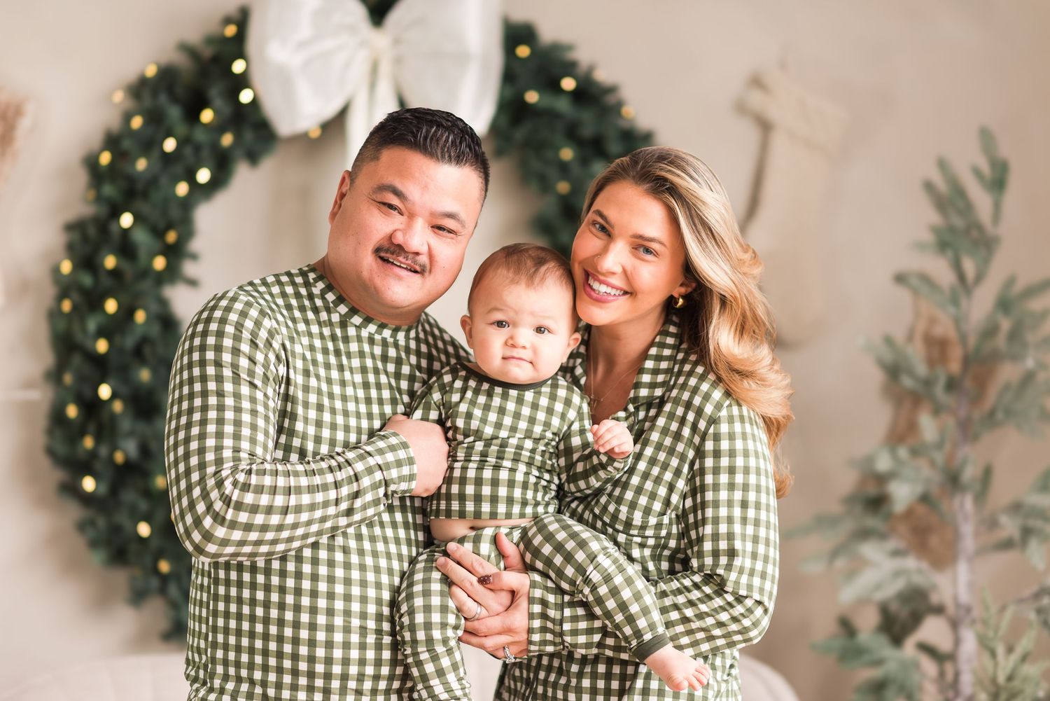 Family wearing matching green gingham outfits poses for Christmas photos with decorated tree in background.