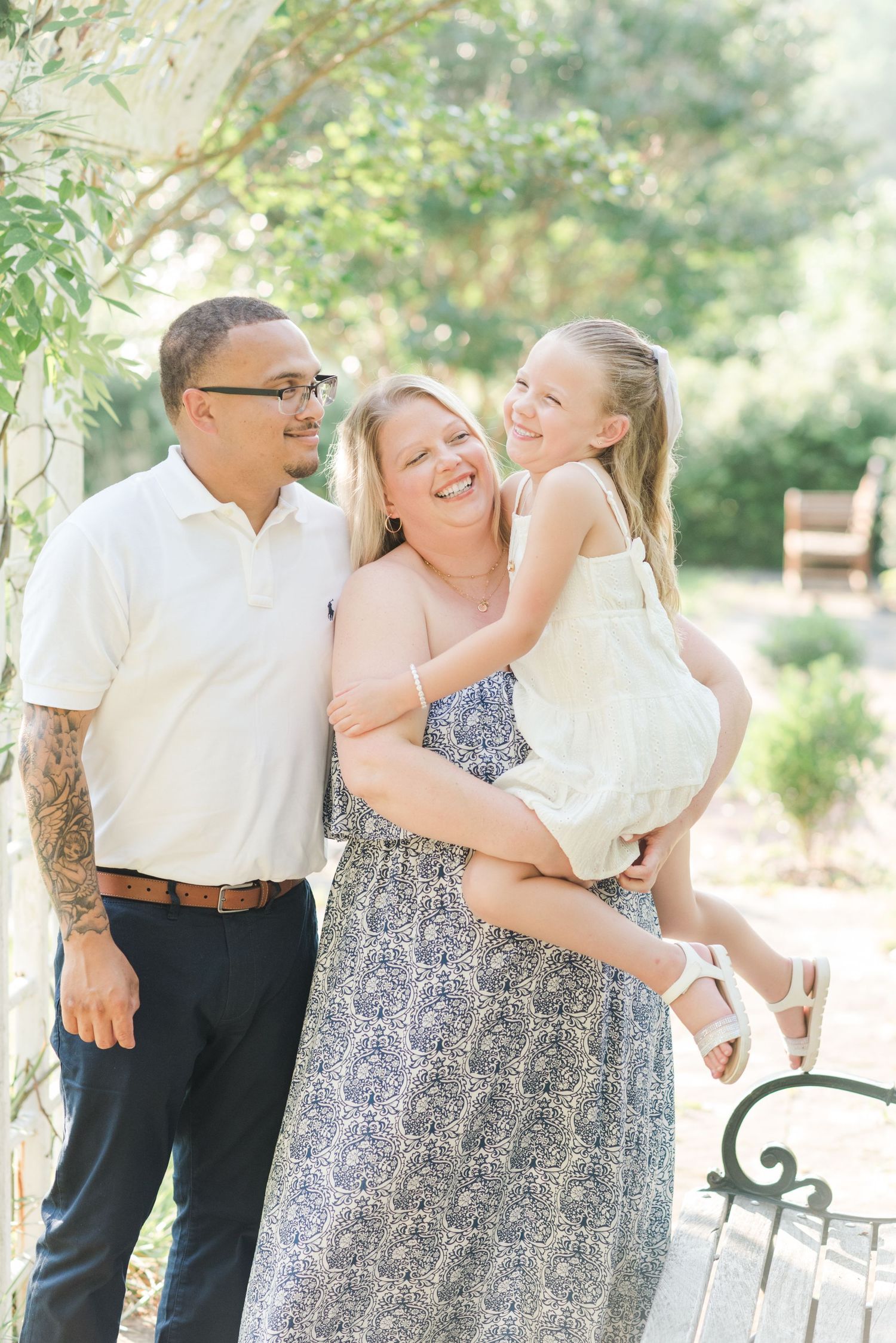 Family members in light summer attire share heartwarming moments in a sun-dappled garden setting.