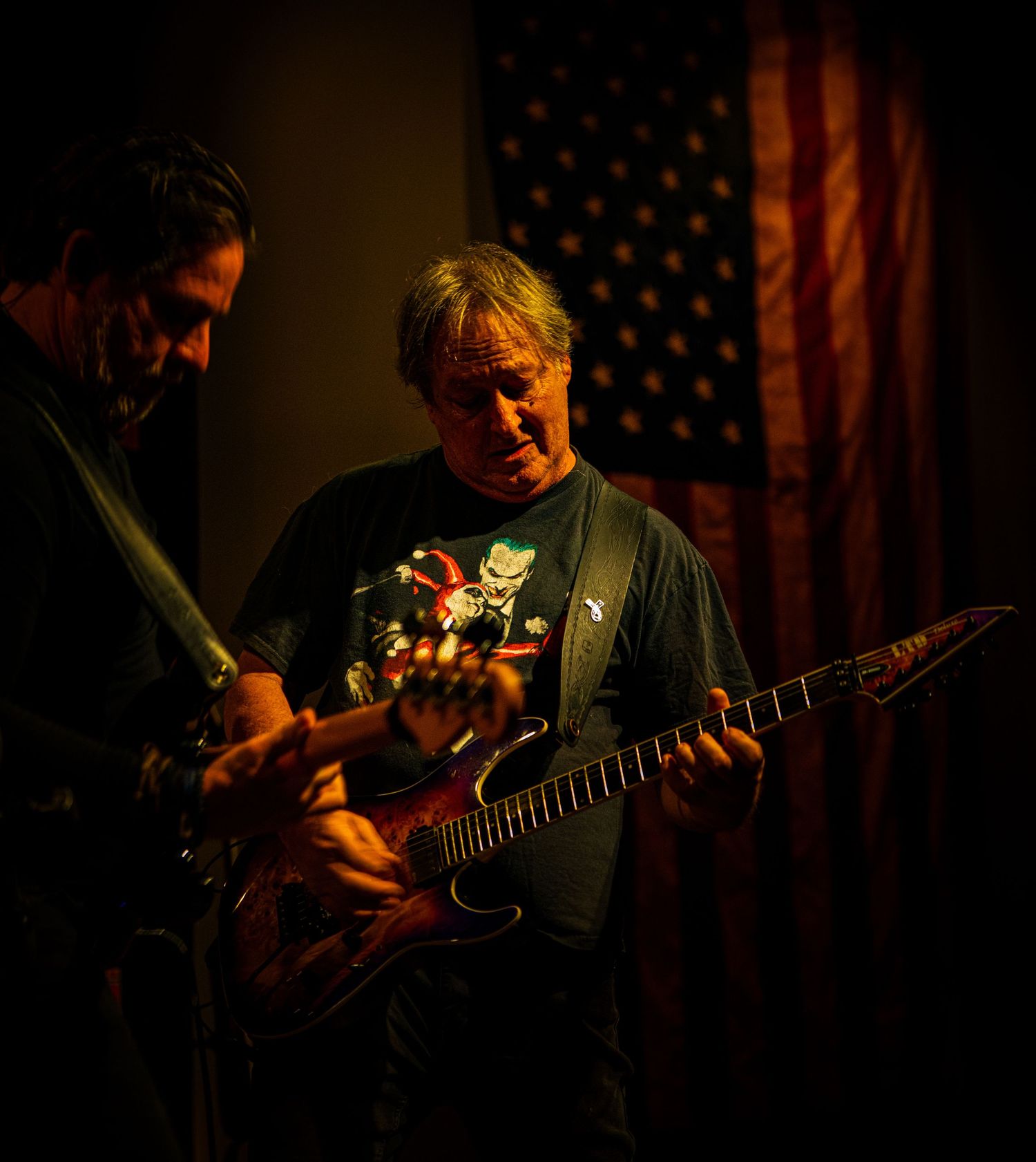 Guitar player performs in dark venue with American flag backdrop.