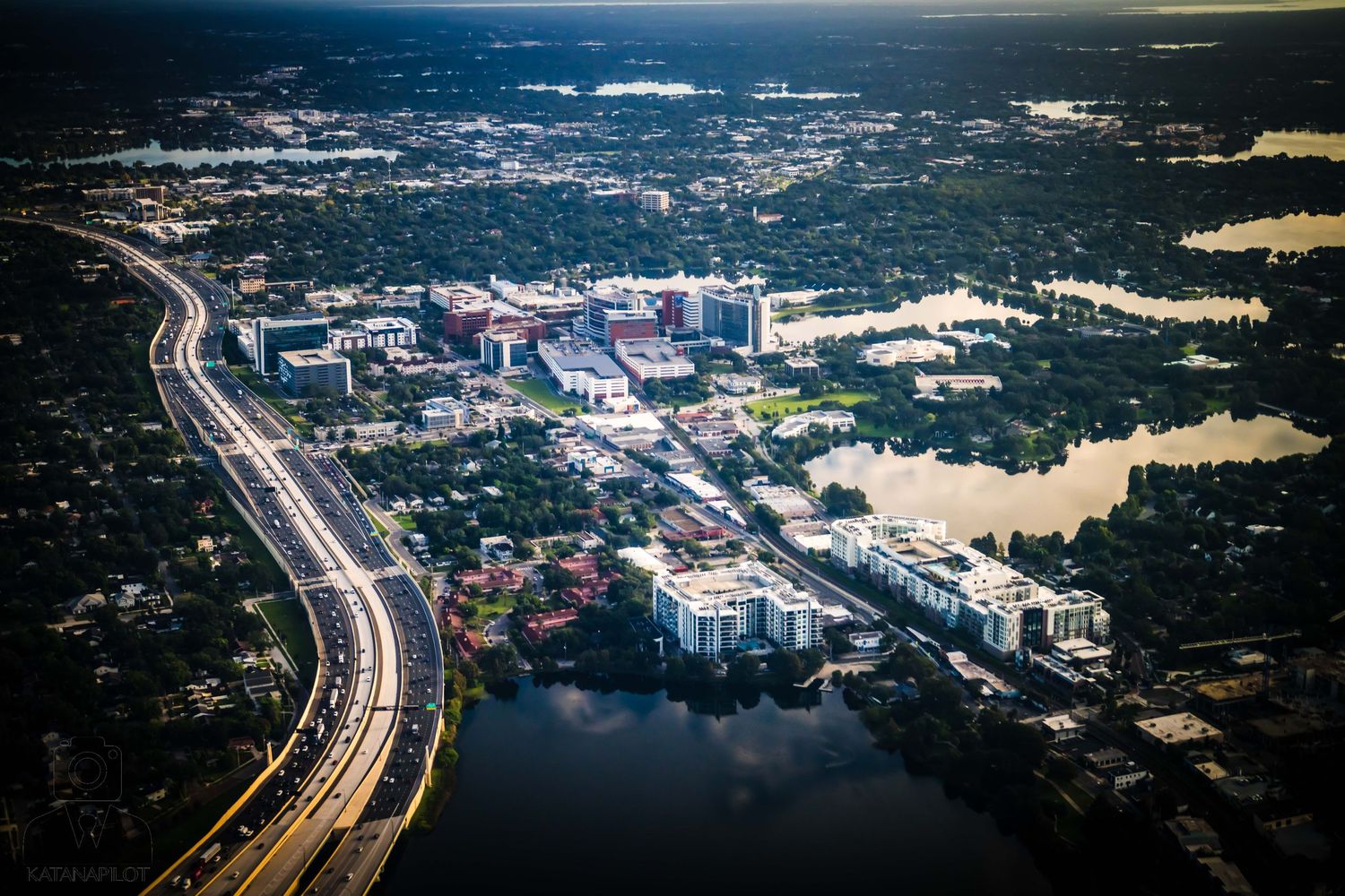 Aerial view of a city development with roads and buildings surrounded by water and greenery.