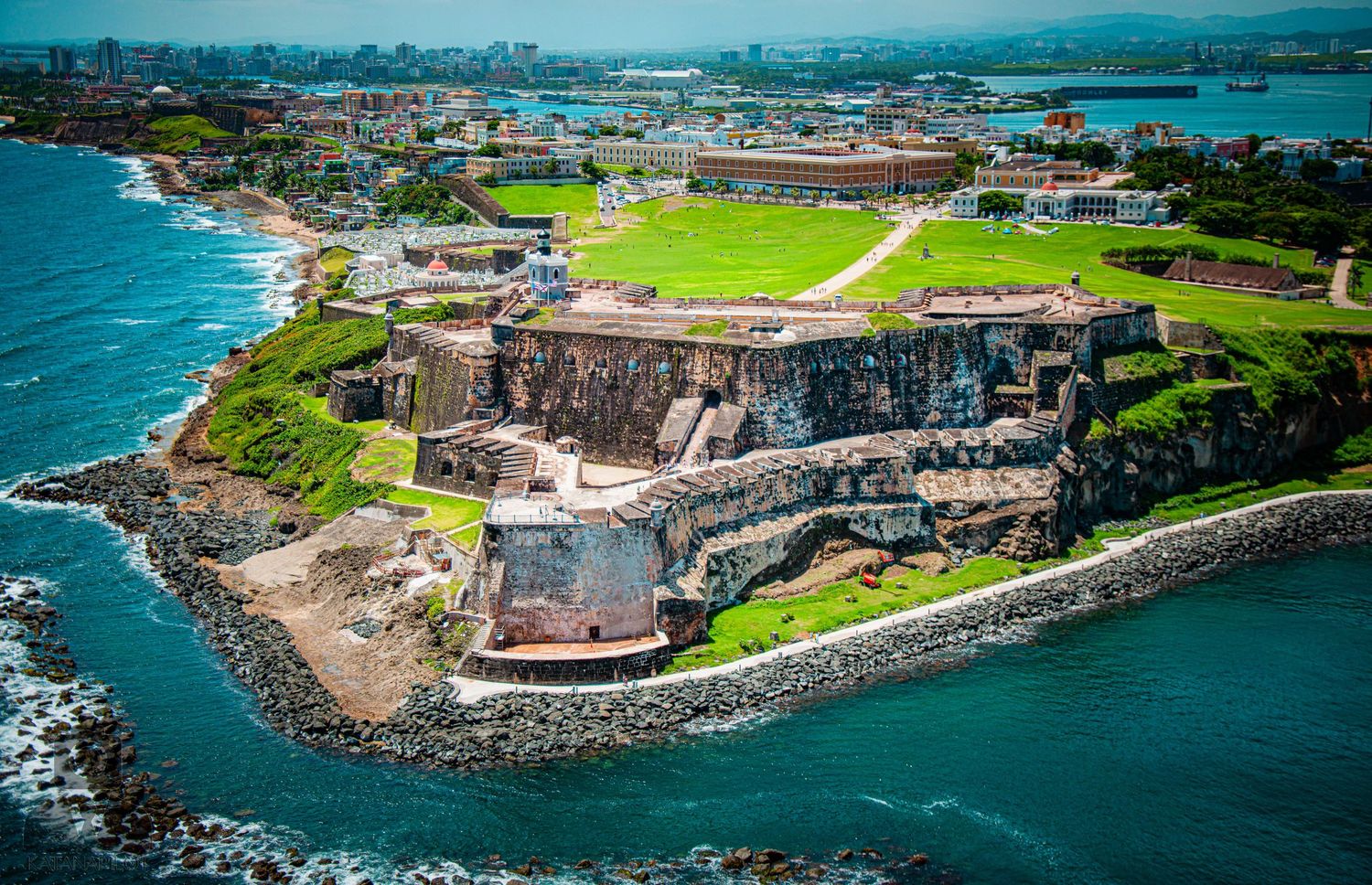 Aerial view of historic coastal fortification with surrounding green fields and rocky shoreline.