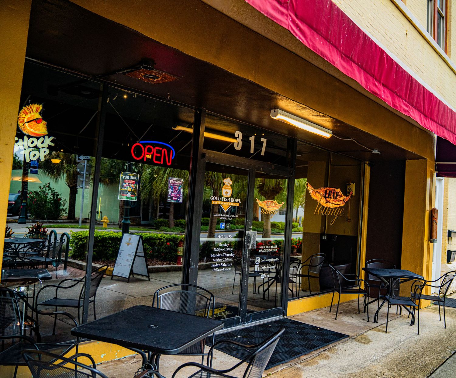 Storefront with pink awning and outdoor seating area along sidewalk.