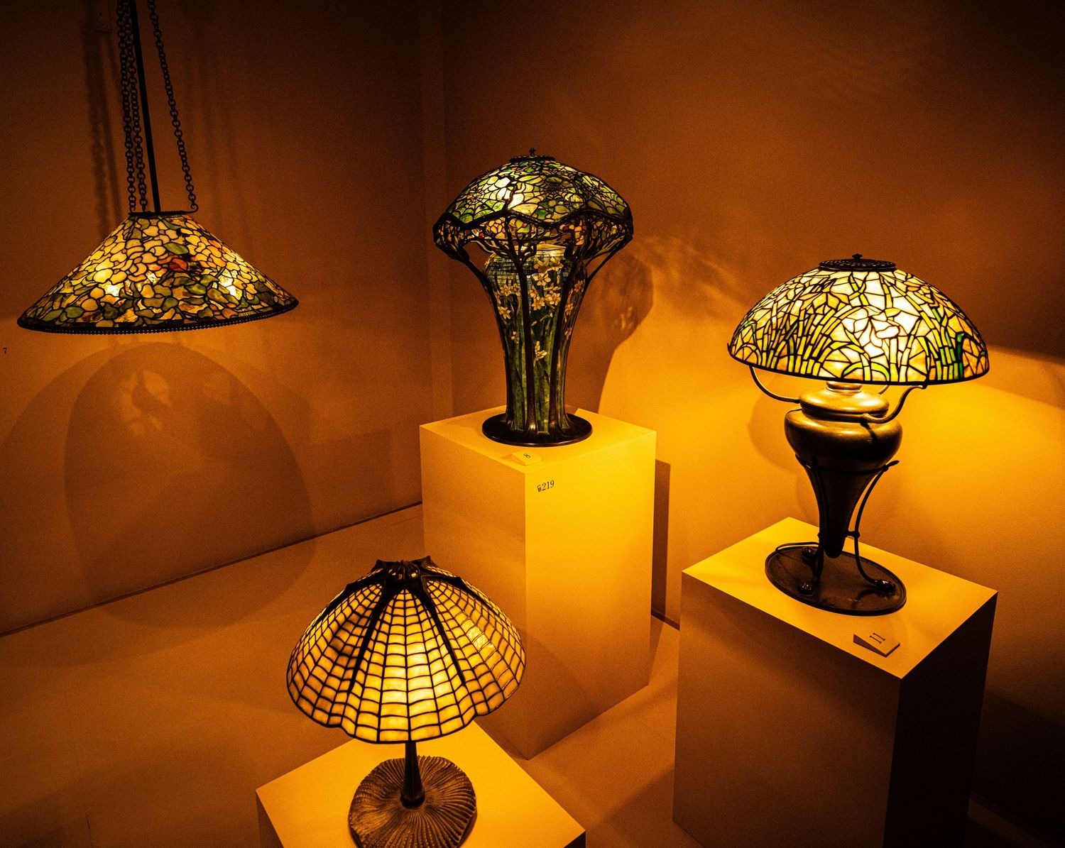 Collection of illuminated Tiffany-style table lamps displayed in a dimly lit museum setting.