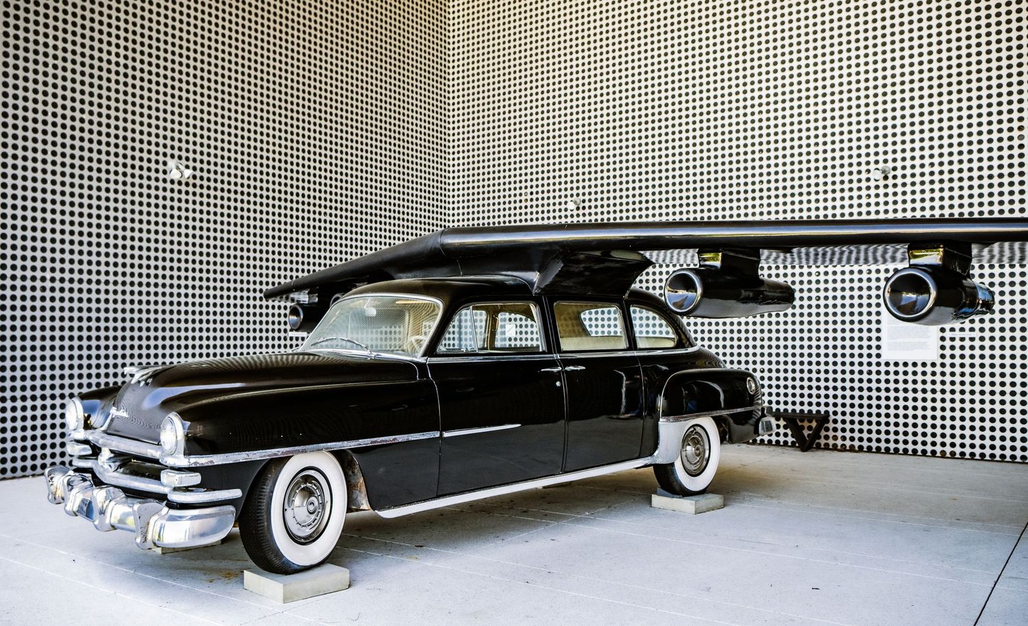 Classic black Cadillac cars from the 1950s displayed in a showroom with white walls and checkered floor pattern.