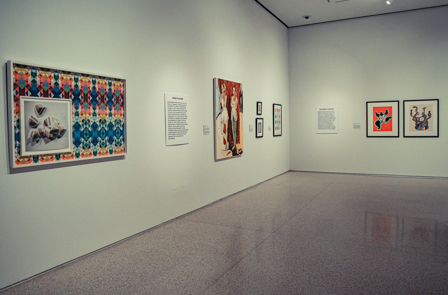 Long gallery hallway with colorful framed artwork displayed along white walls under track lighting.