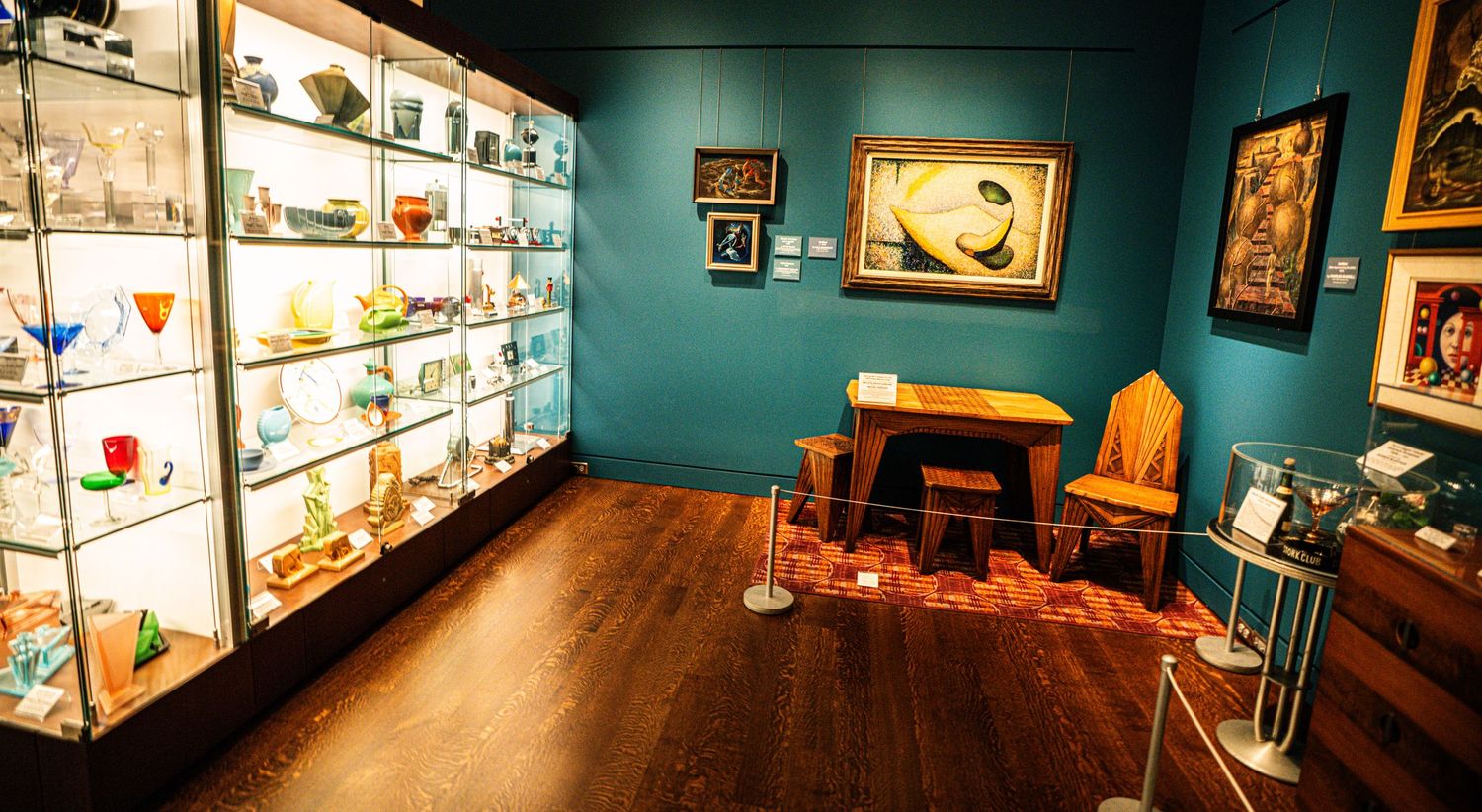 Panoramic view of illuminated display cases filled with collectibles in a museum with teal walls and wooden floors.