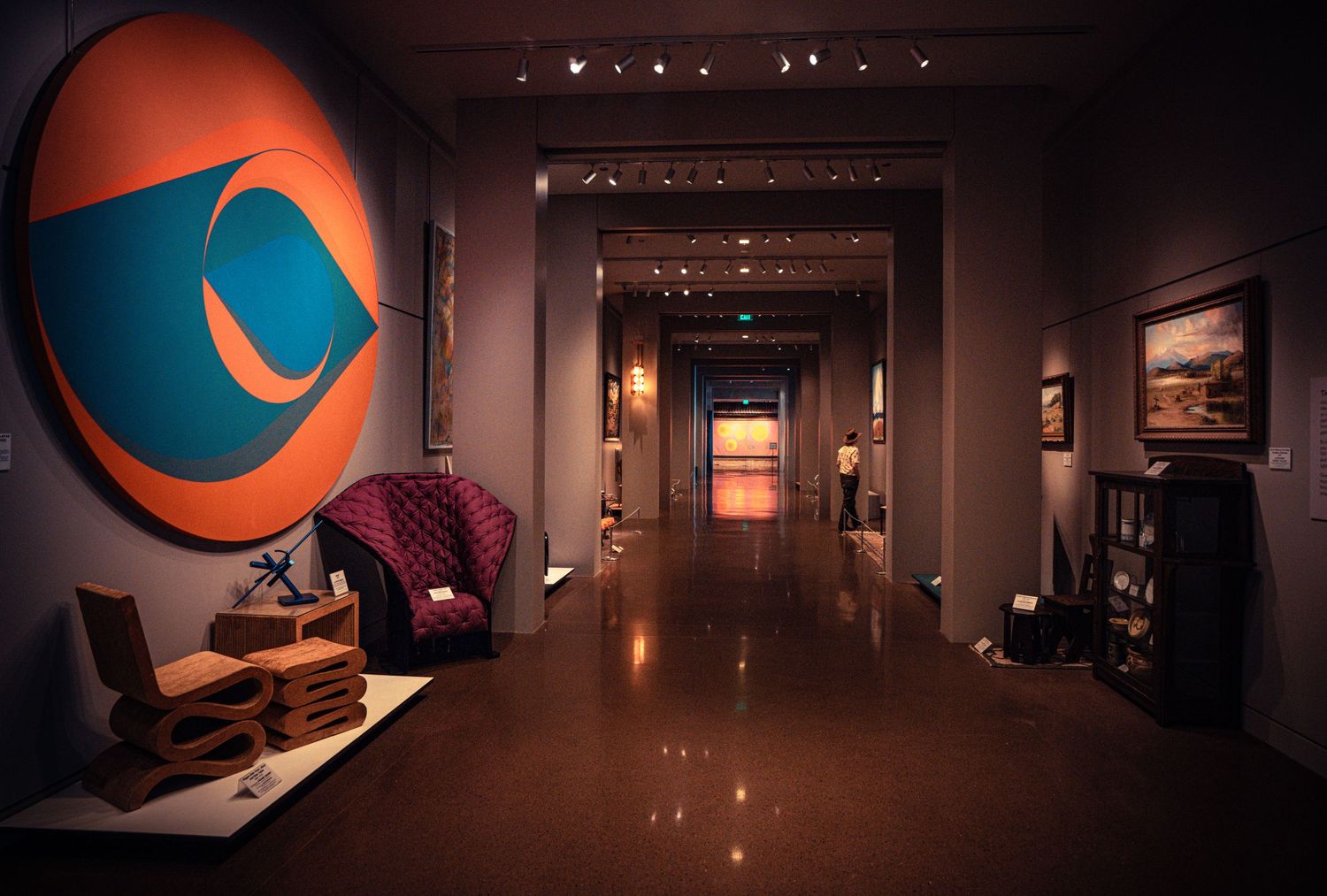 Dimly lit luxurious hotel hallway with red velvet chairs and modern art featuring a large blue circular logo on the wall.