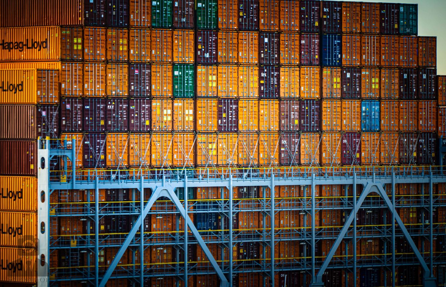 Illuminated shipping containers stacked at a port terminal create a colorful geometric pattern at night.