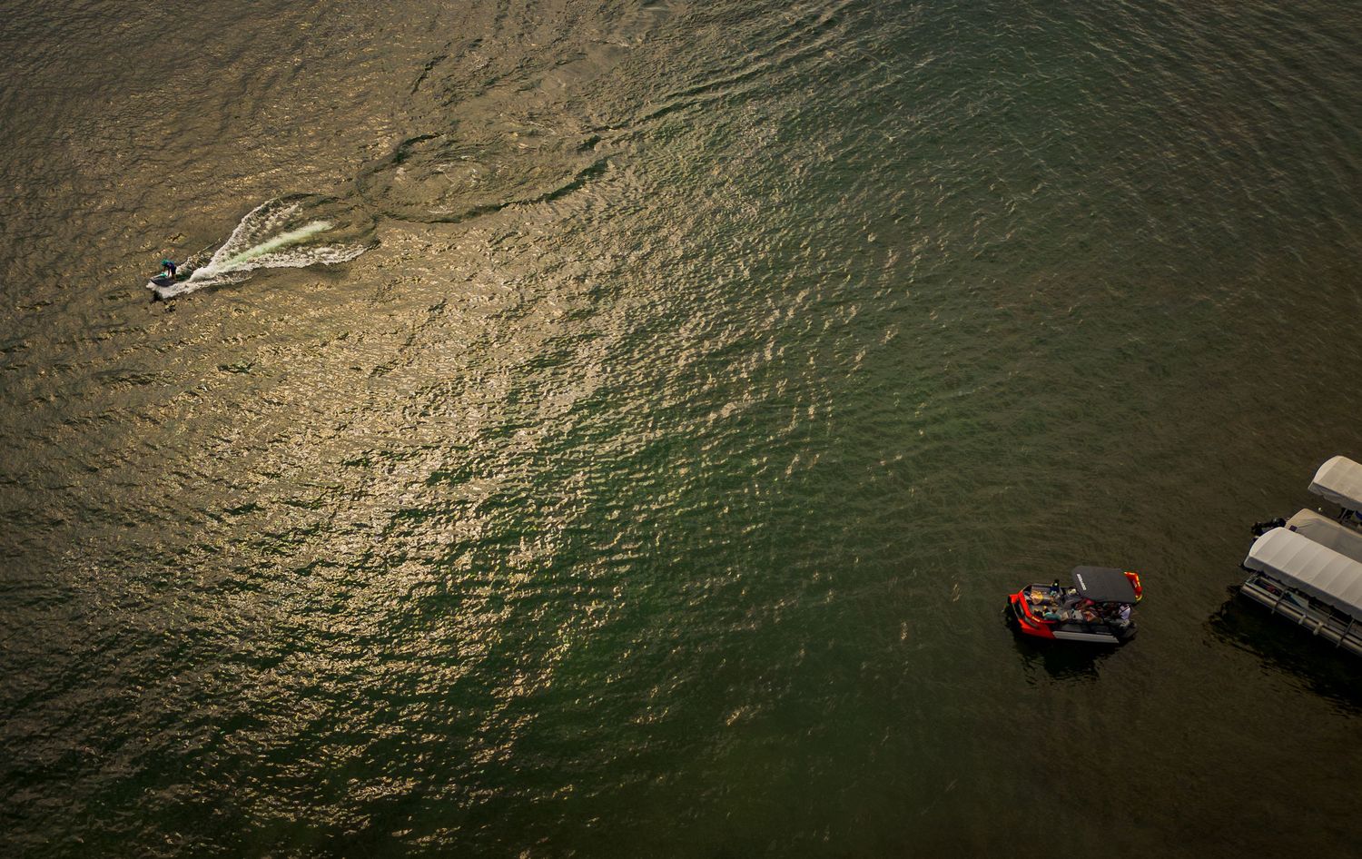 Aerial view of boats creating wakes in dark green water.