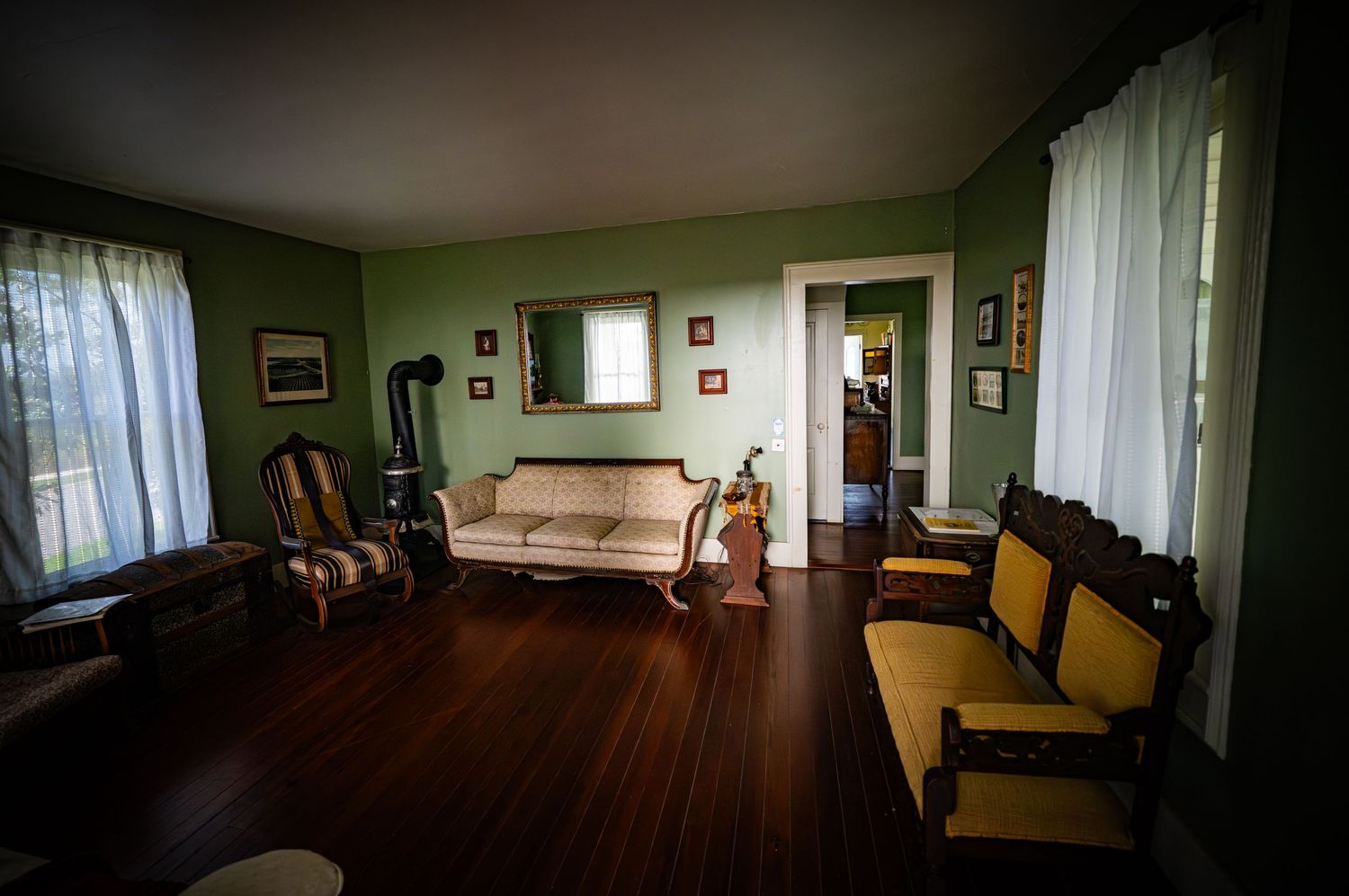 Formal parlor with green walls, antique furniture, and hardwood floors in a historic home.