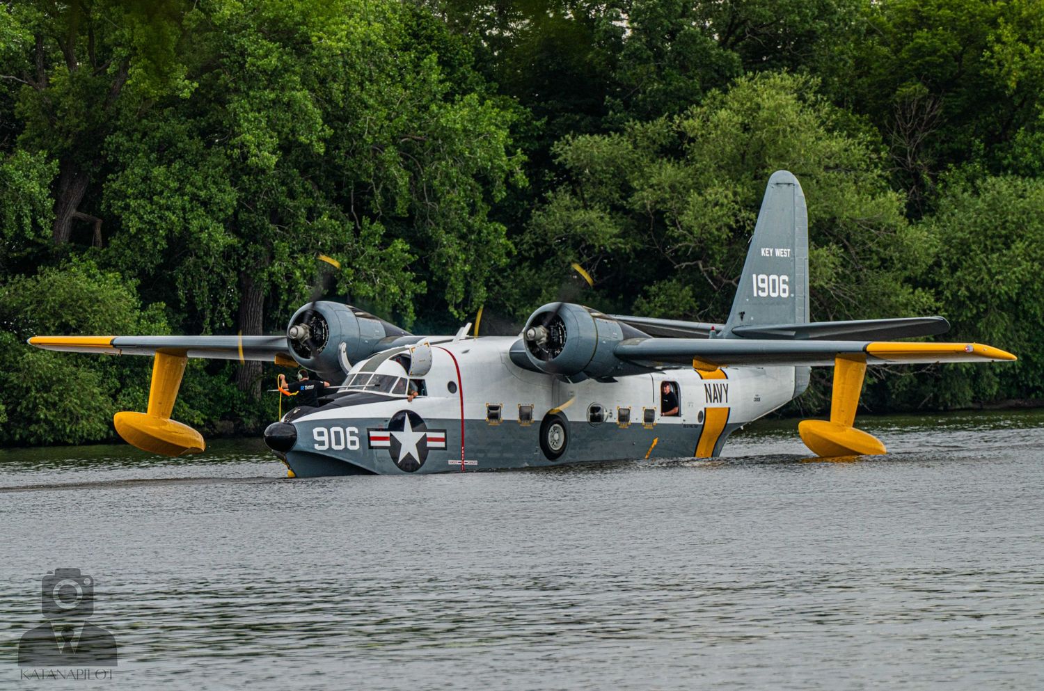 Vintage military aircraft displayed on floats in a lake setting.