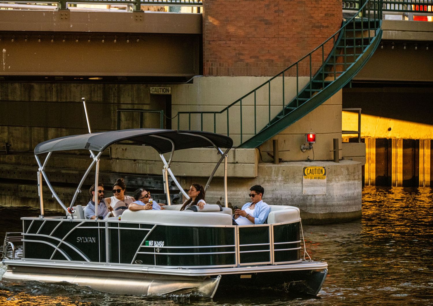 Pontoon boats and small watercraft docked along a brick waterfront during sunset.