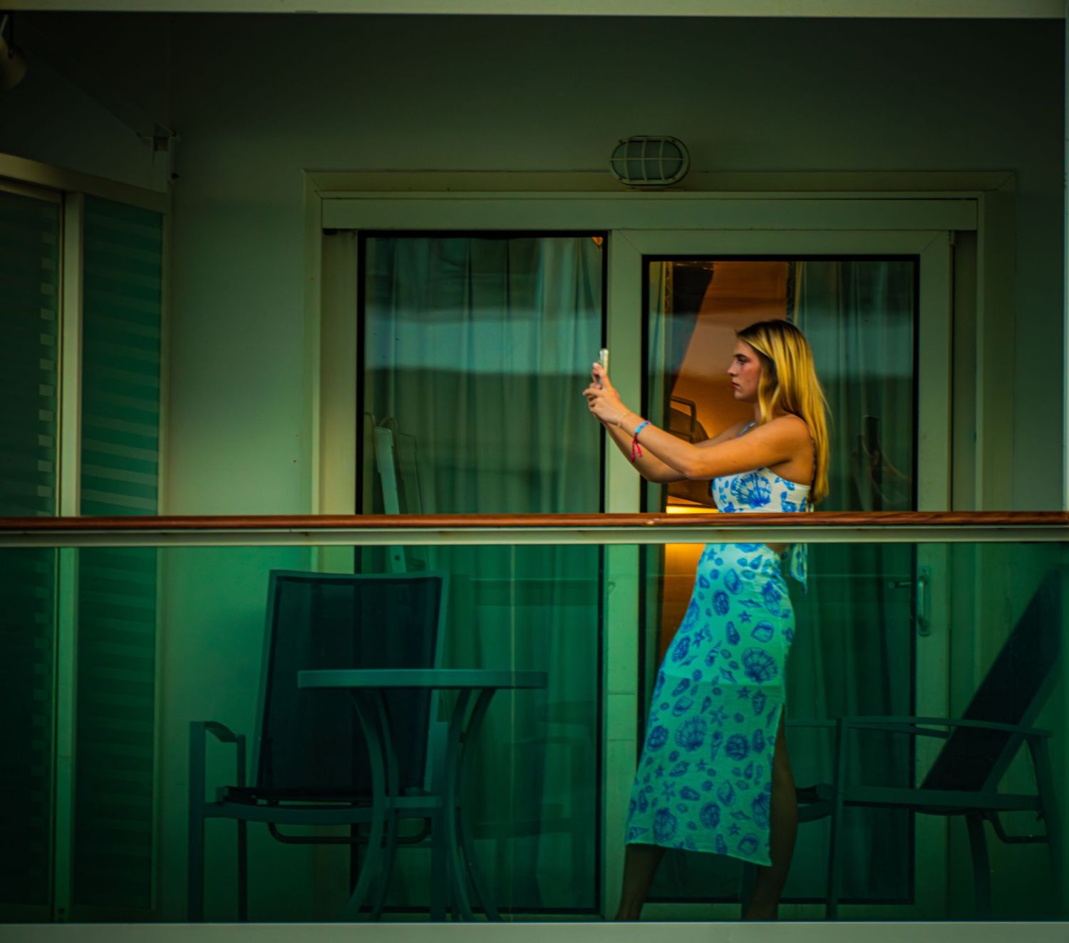 Person in a turquoise floral dress takes a selfie on a cruise ship balcony with green-tinted lighting.