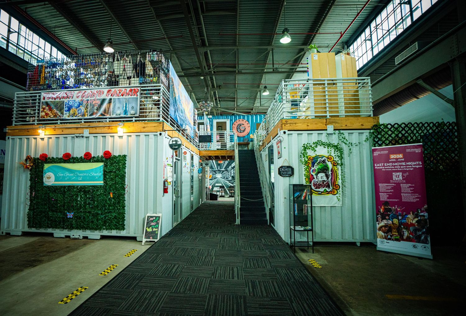 Industrial warehouse converted into a vibrant pop-up market with shipping containers, green walls, and festive decorations.