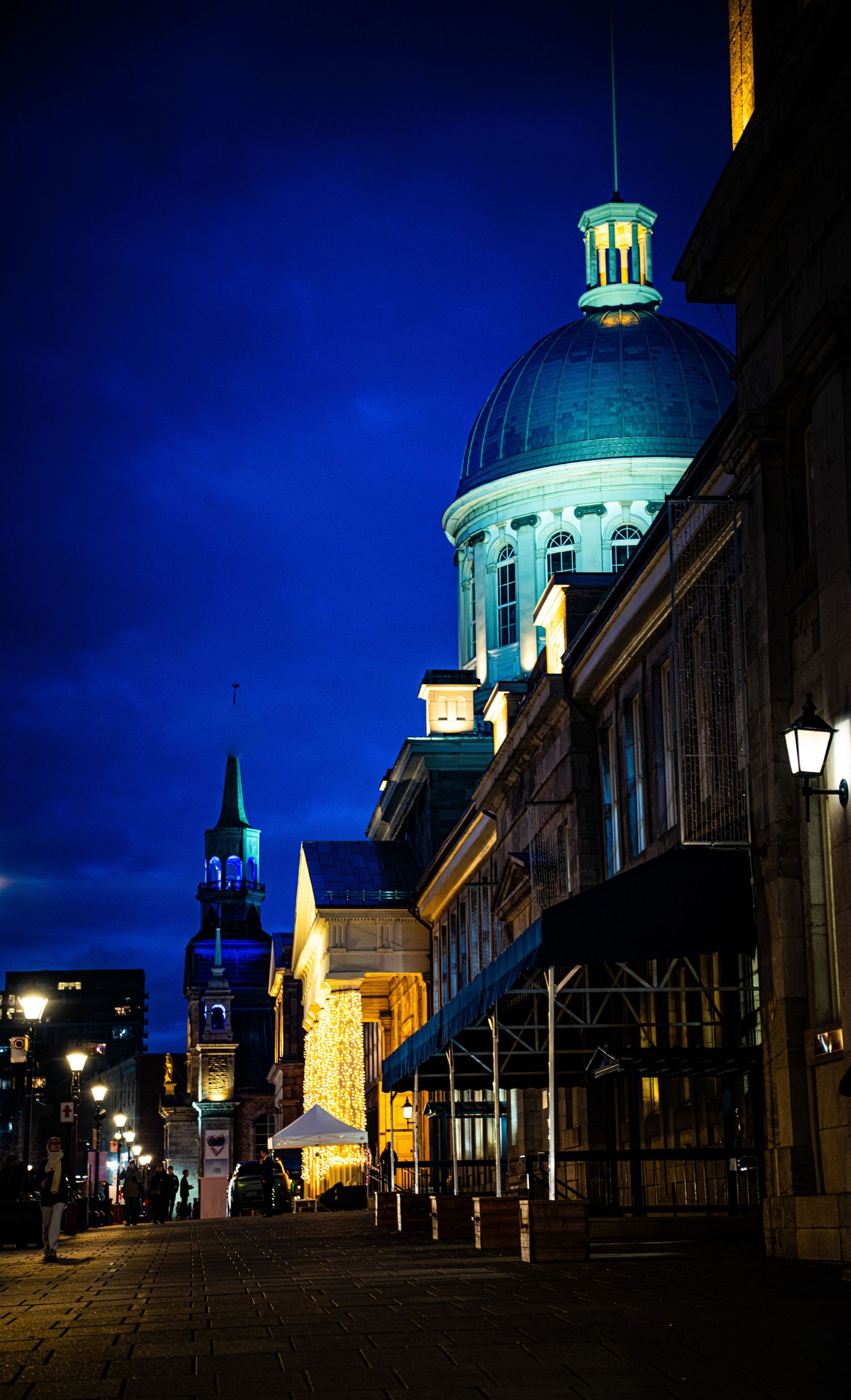Historic Old Montreal street illuminated at night with glowing domes and lampposts casting a blue and golden ambiance.
