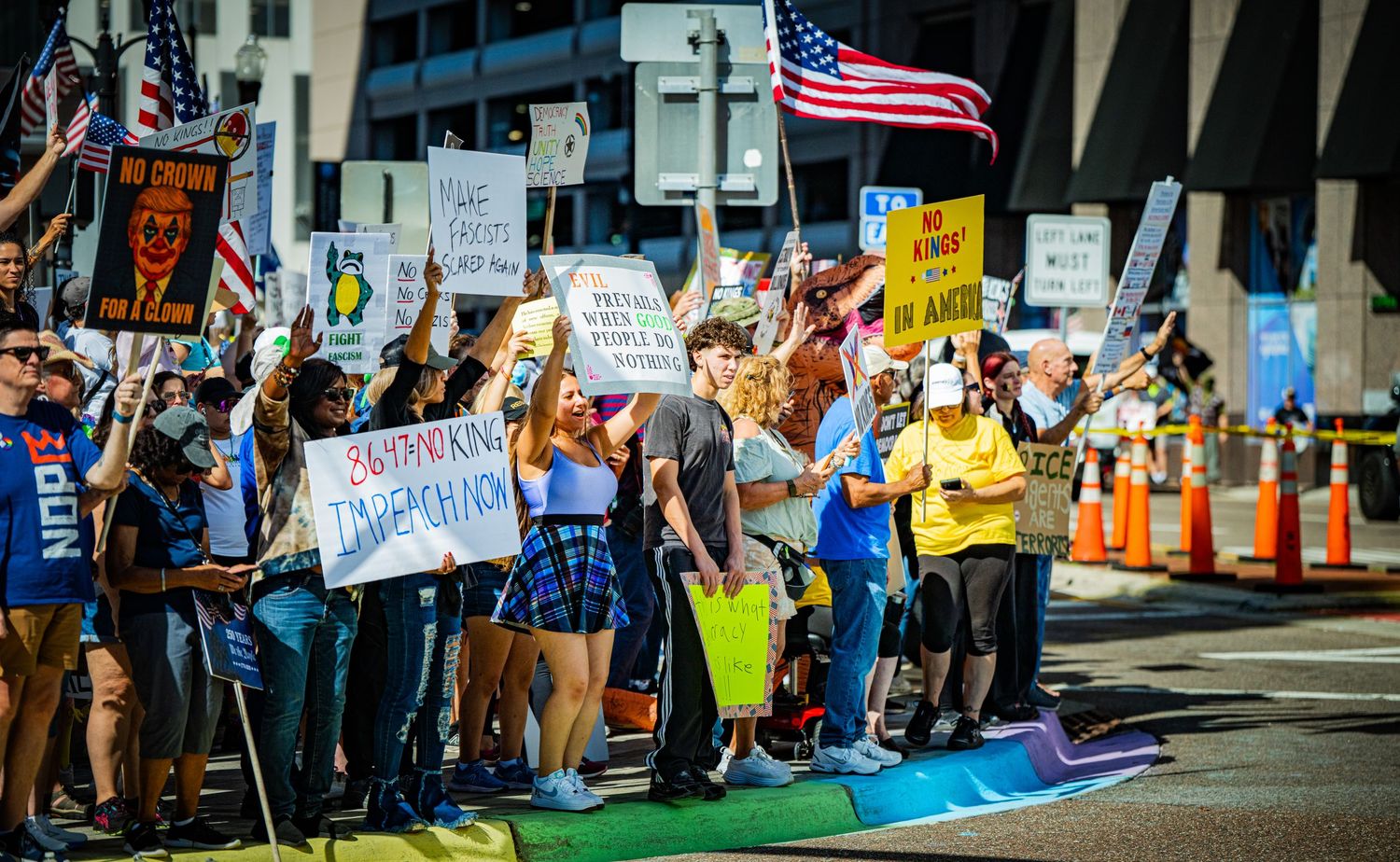 American flags and protest signs fill a crowded city sidewalk during a demonstration.