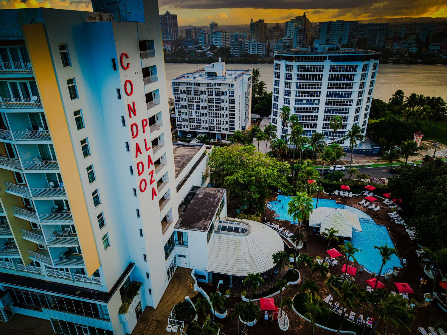 Sunset view of colorful high-rise apartment buildings with swimming pools and landscaped gardens near ocean.