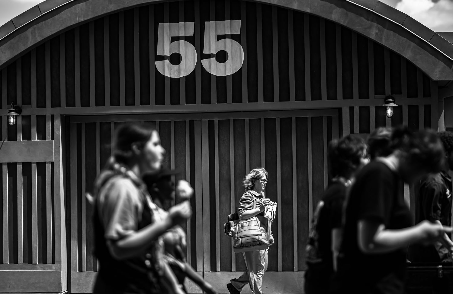 People gather beneath a large number 55 on an arched building exterior in black and white photography.