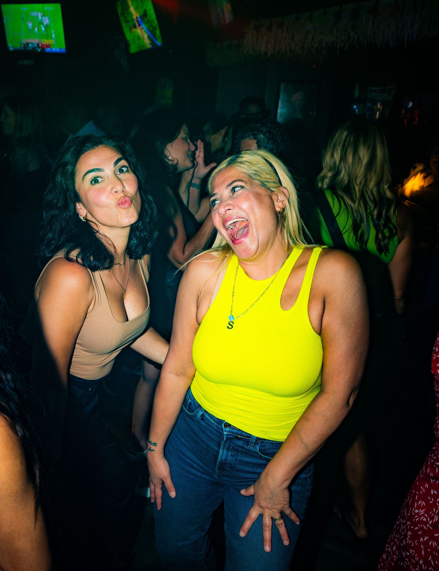 Two friends having fun and making silly faces at a nightclub with green lighting.