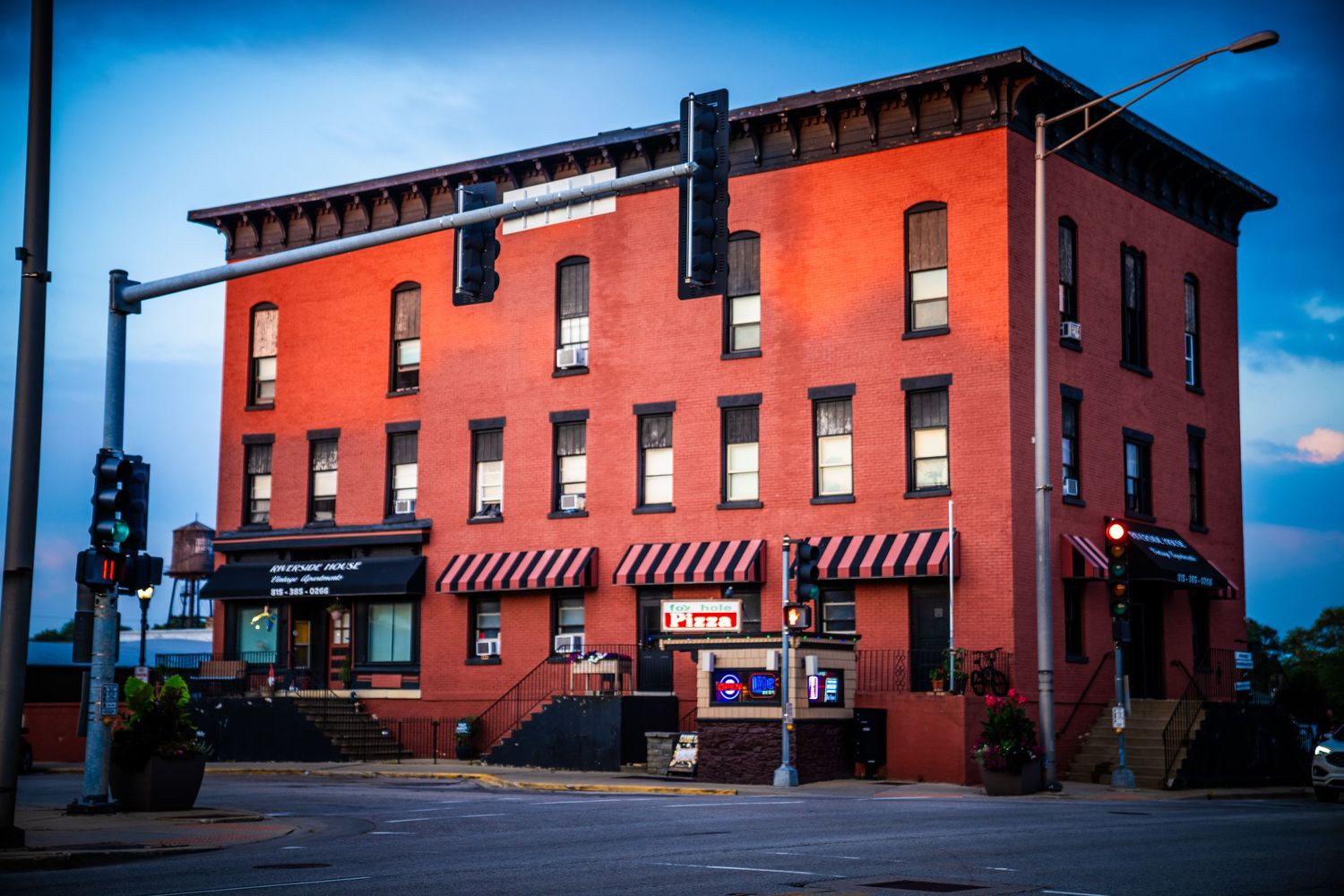 Historic red brick building with striped awnings stands on a corner under blue sky in downtown McHenry.