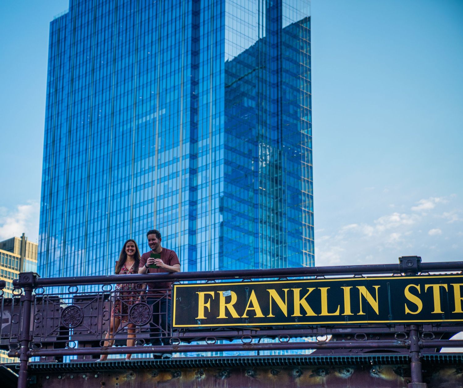 Franklin Street sign mounted on bridge with blue glass skyscraper towering in background.