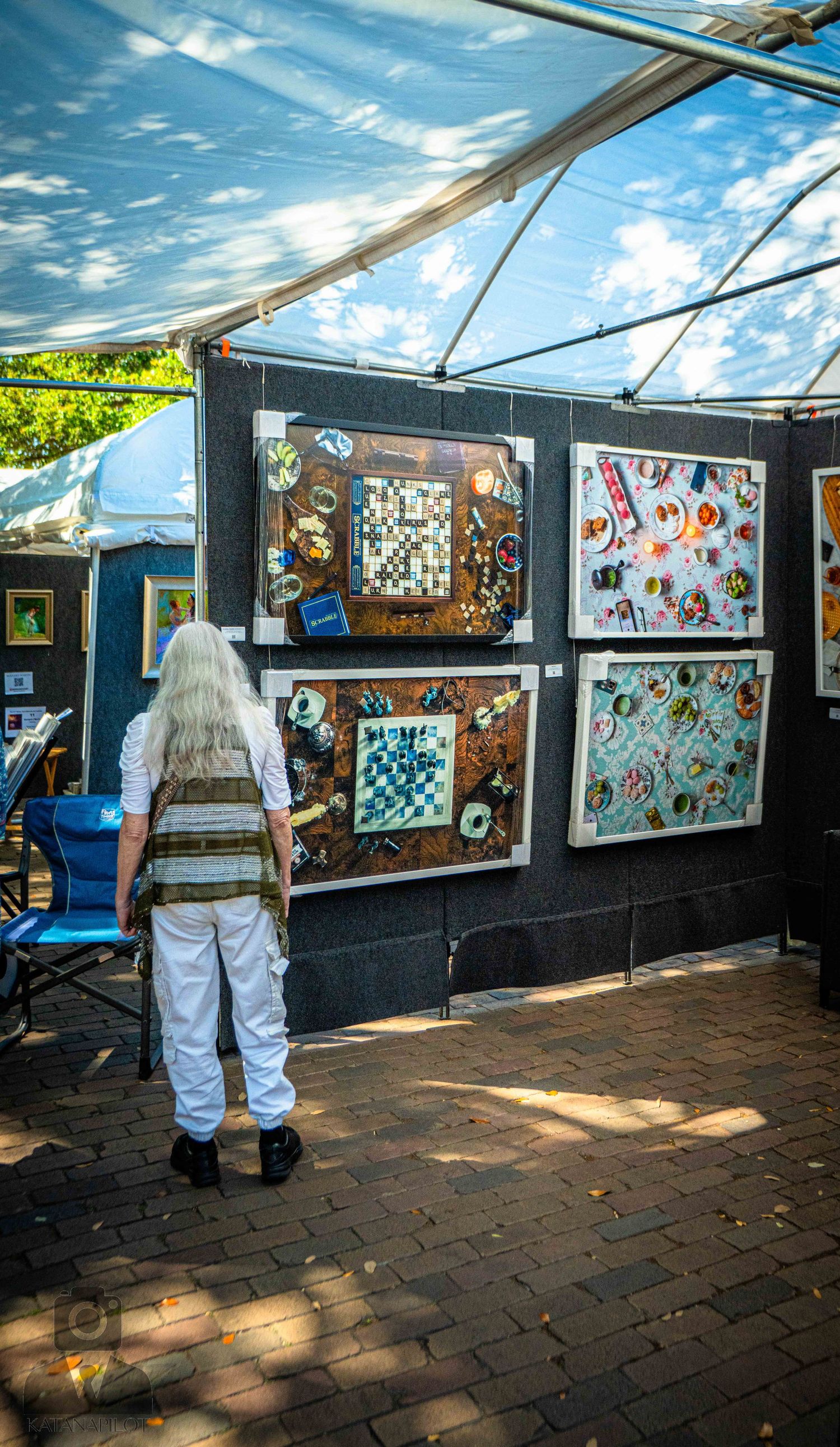 Art gallery display showing colorful artwork mounted on black panels under a covered outdoor walkway.
