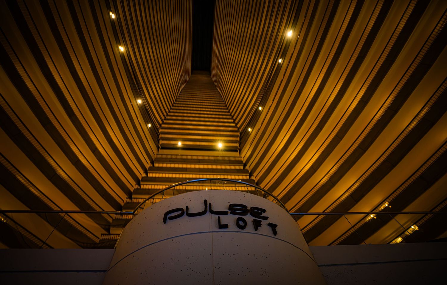 Pulse Loft sign illuminated at night with dramatic golden architectural lines converging upward in a modern building interior.