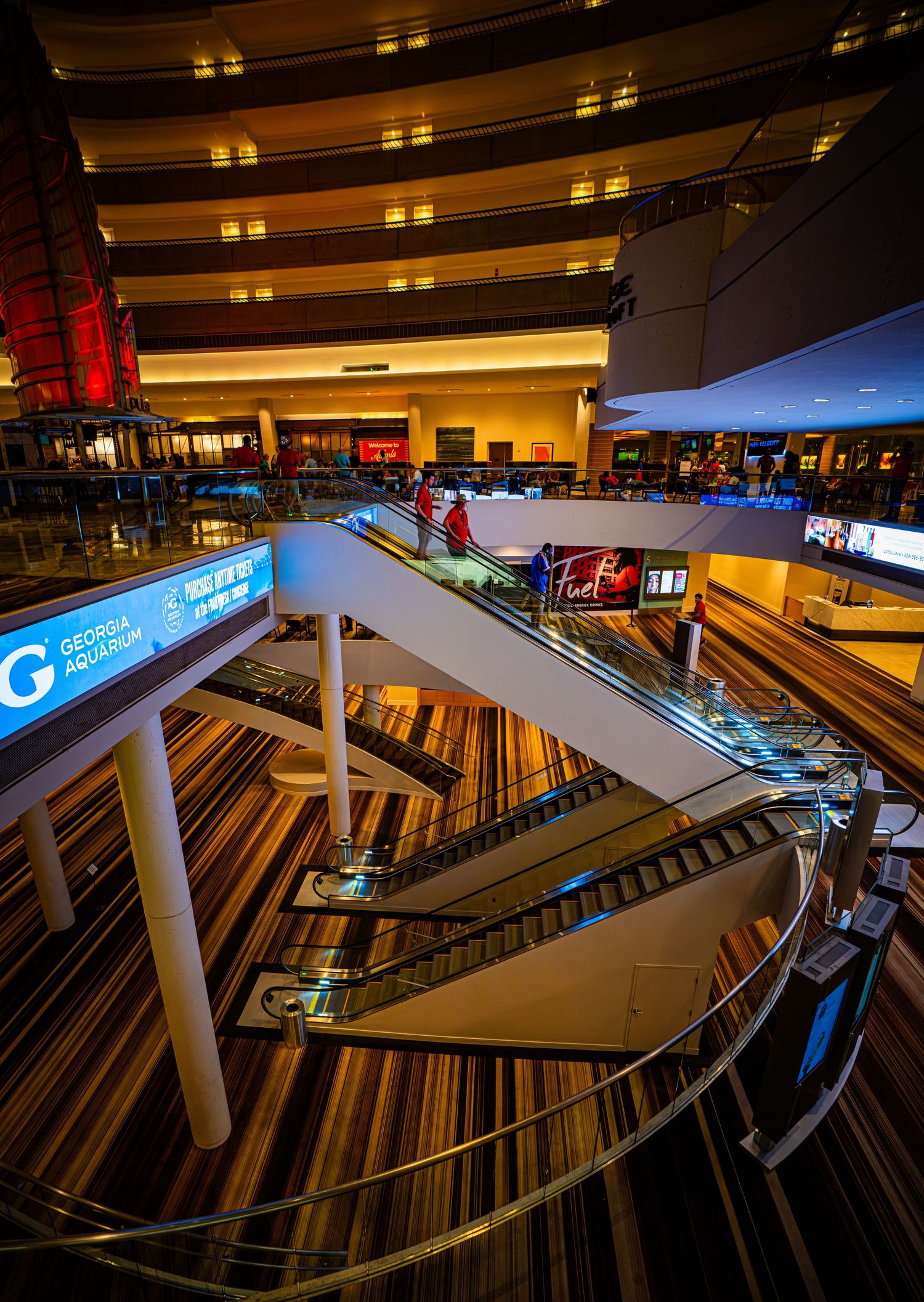 Interior view of Georgia Aquarium atrium featuring escalators, striped floors, and multi-level architecture with warm ambient lighting.