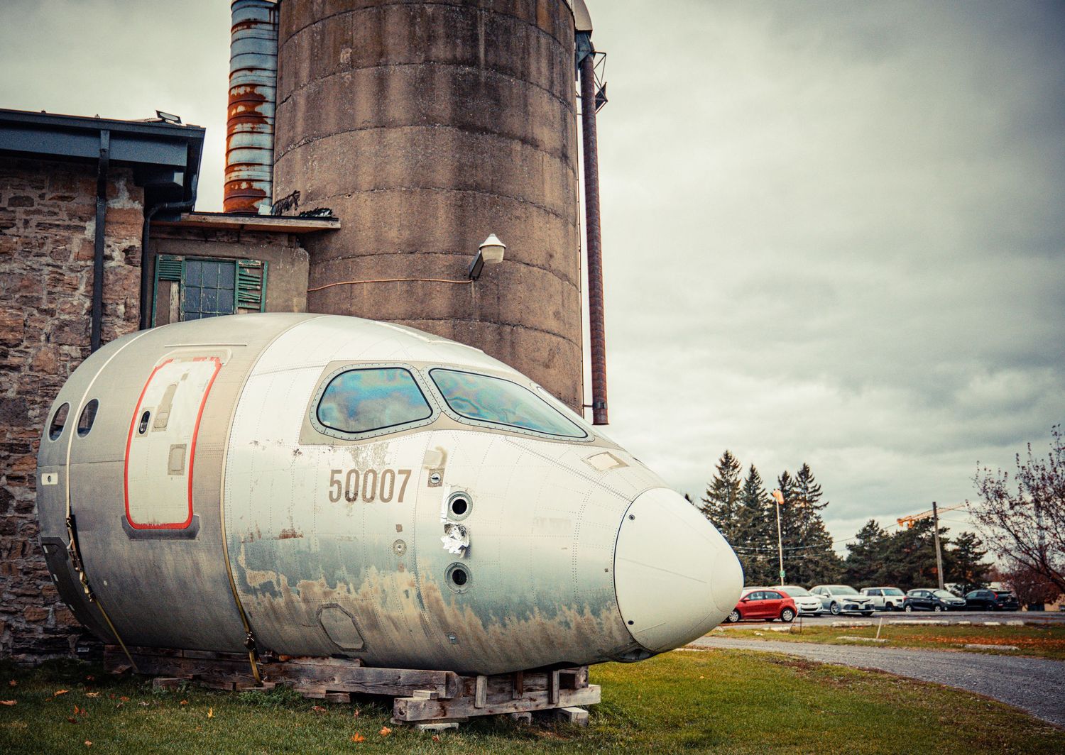 Decommissioned aircraft fuselage resting on ground near industrial storage silos.